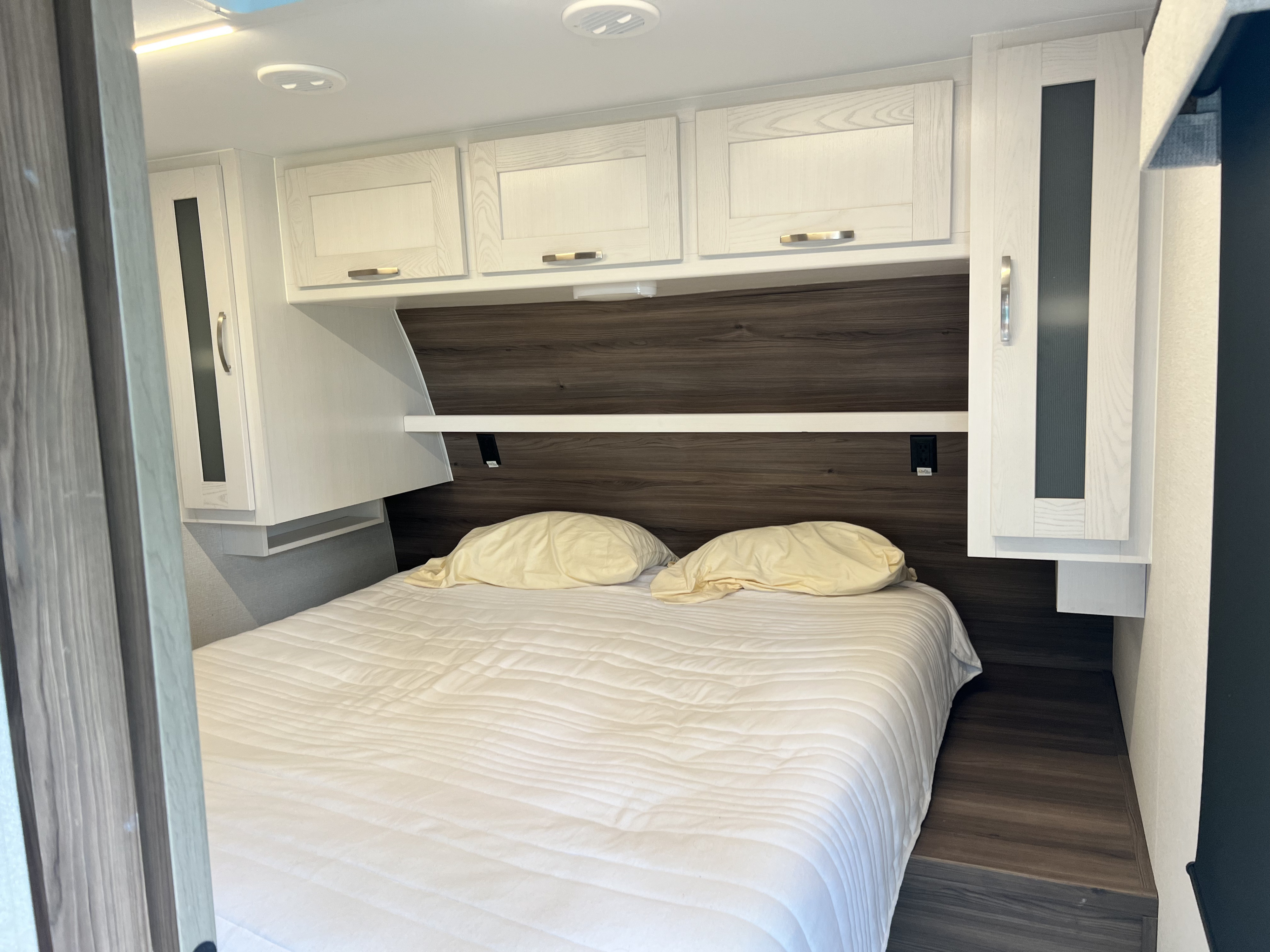 Sleek RV rental bedroom: features a comfy bed, bright white cabinets, and dark wood headboard for a relaxing stay.. Cruiser RV x252 Go Explore 2025