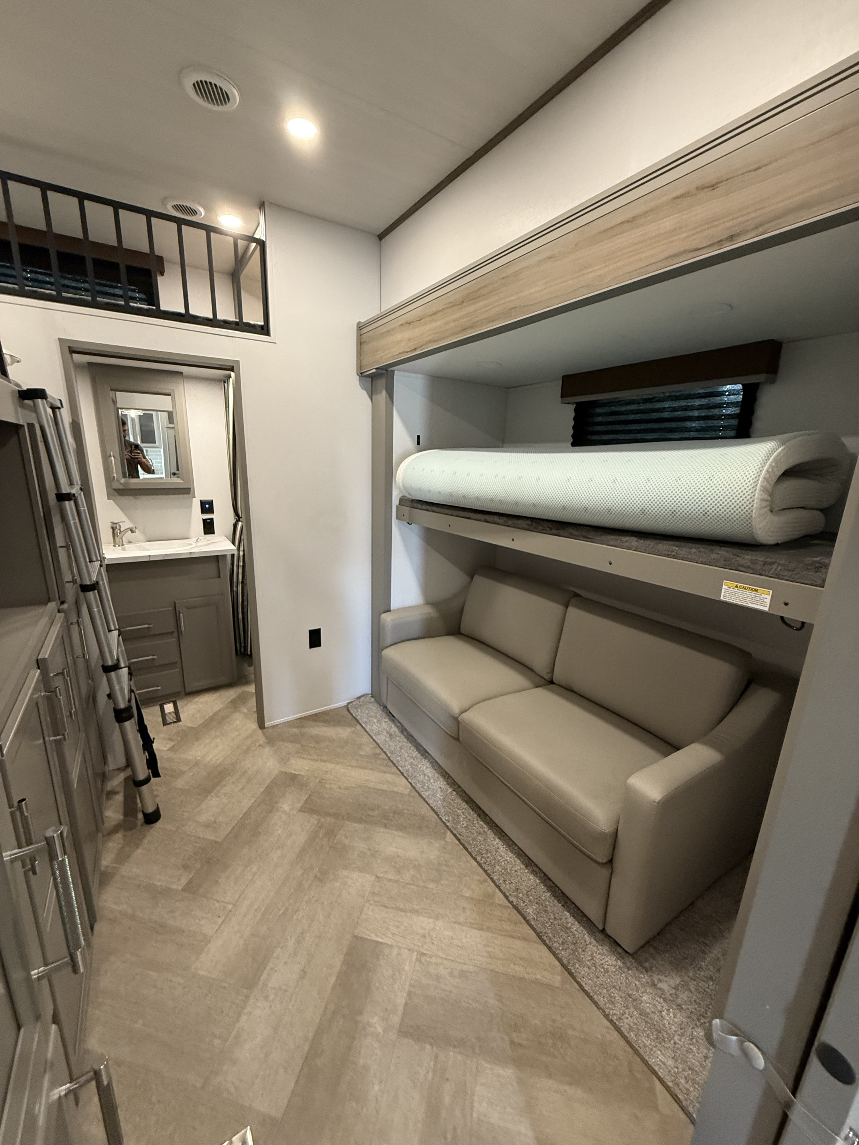 Explore this modern RV rental interior featuring a bunk bed with sofa, bathroom vanity, and loft area, designed for compact living.. Keystone Sprinter Wide Body 2025