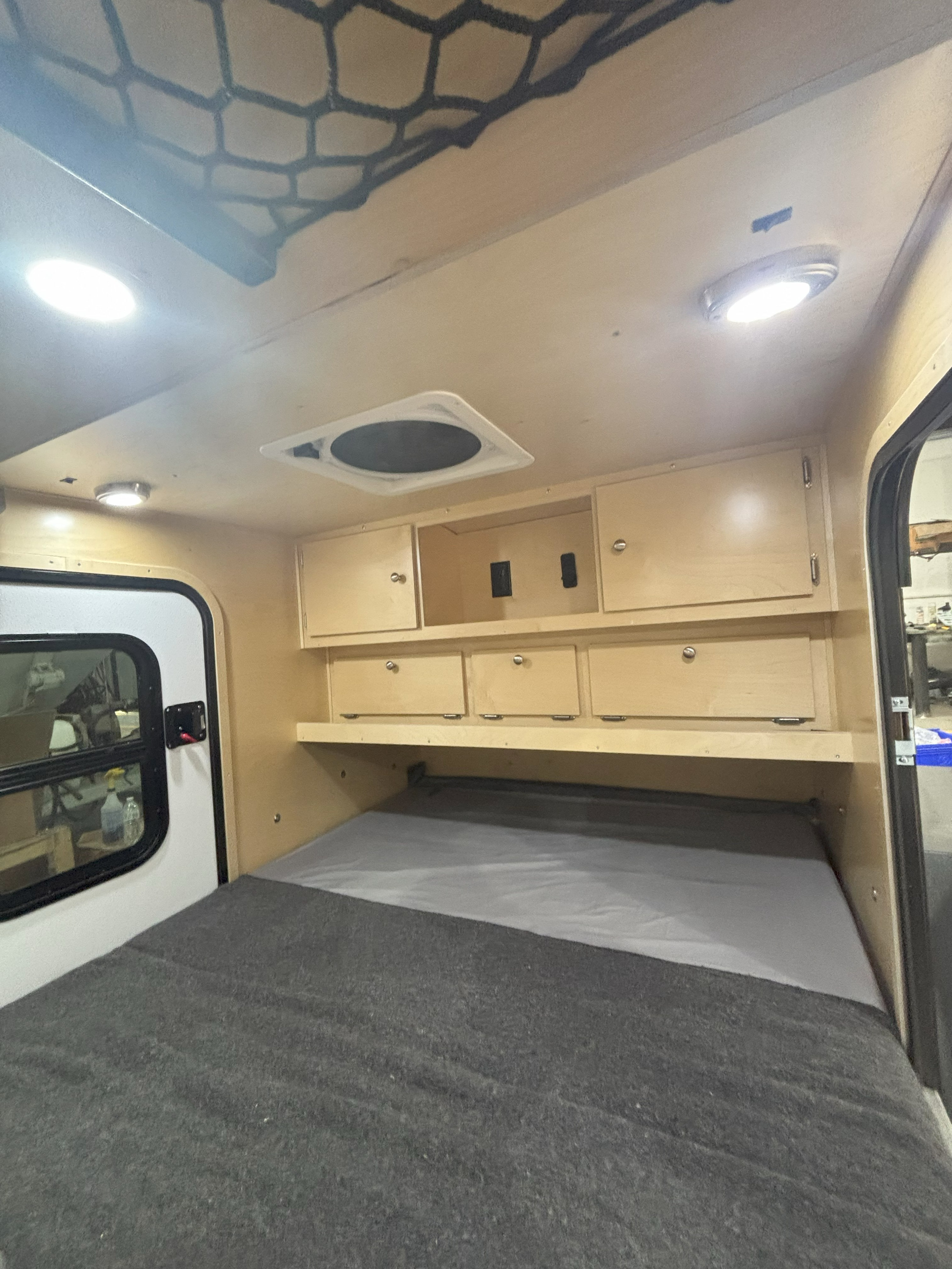 RV rental's cozy interior: features a bed, wooden cabinets, ceiling lights, and a fan, ready for your next adventure.. Teardrops NW Scout 2024