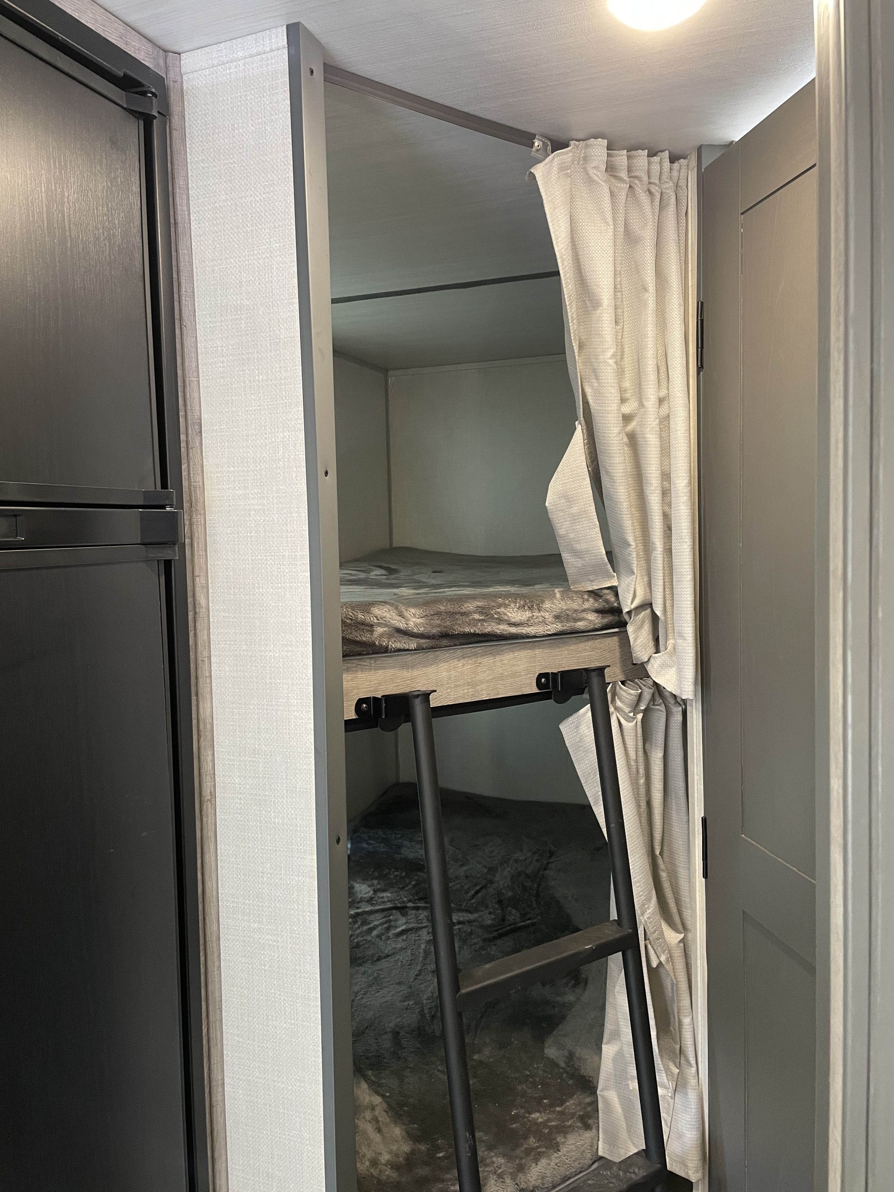 This RV rental interior showcases cozy bunk beds with privacy curtains and an adjacent refrigerator, perfect for compact living.. Forest River Surveyor Legend 2023