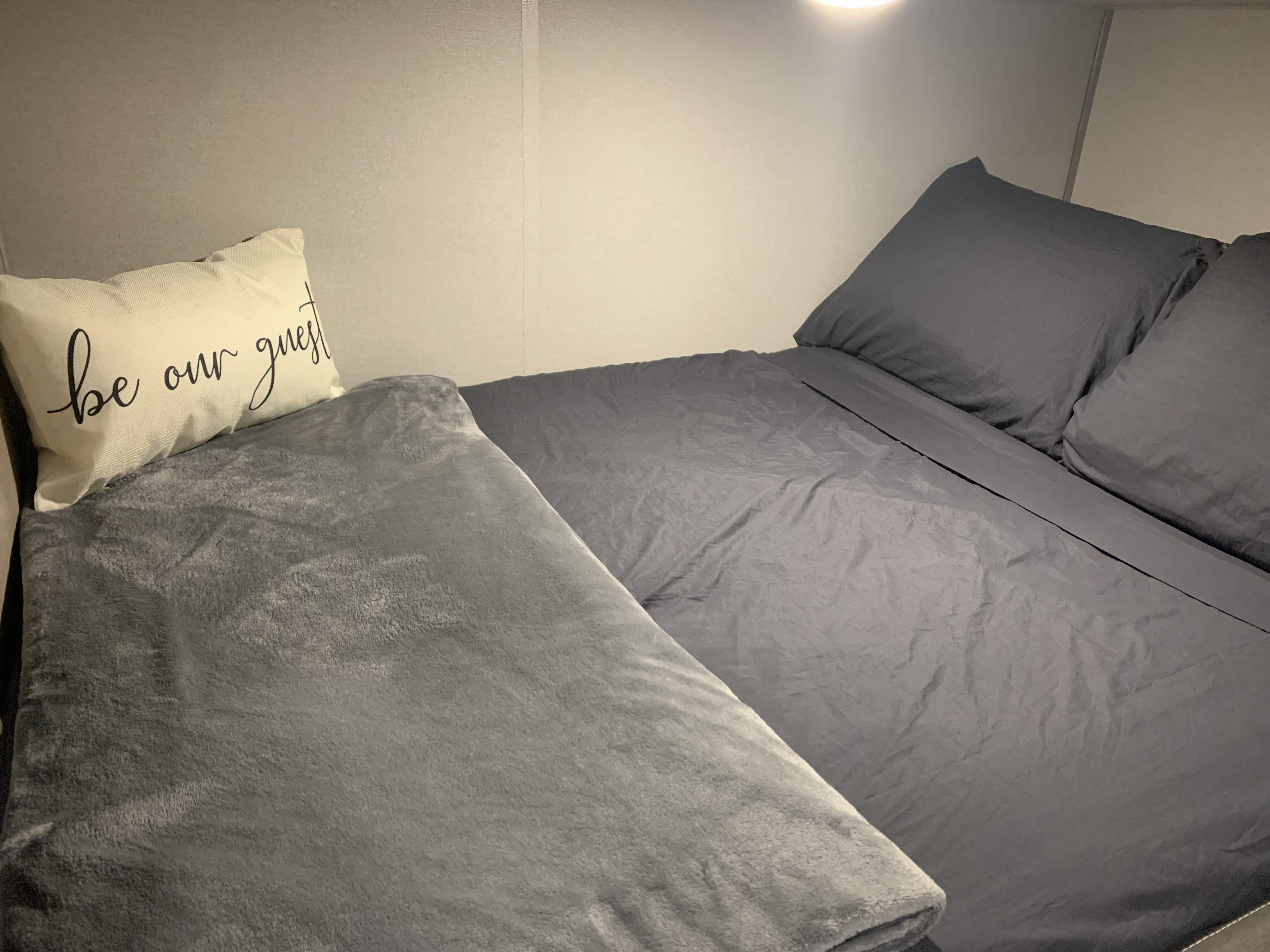 Cozy RV rental bedroom with two beds, soft blankets, and a welcoming "be our guest" pillow.. Forest River Aurora Aurora Light 2024
