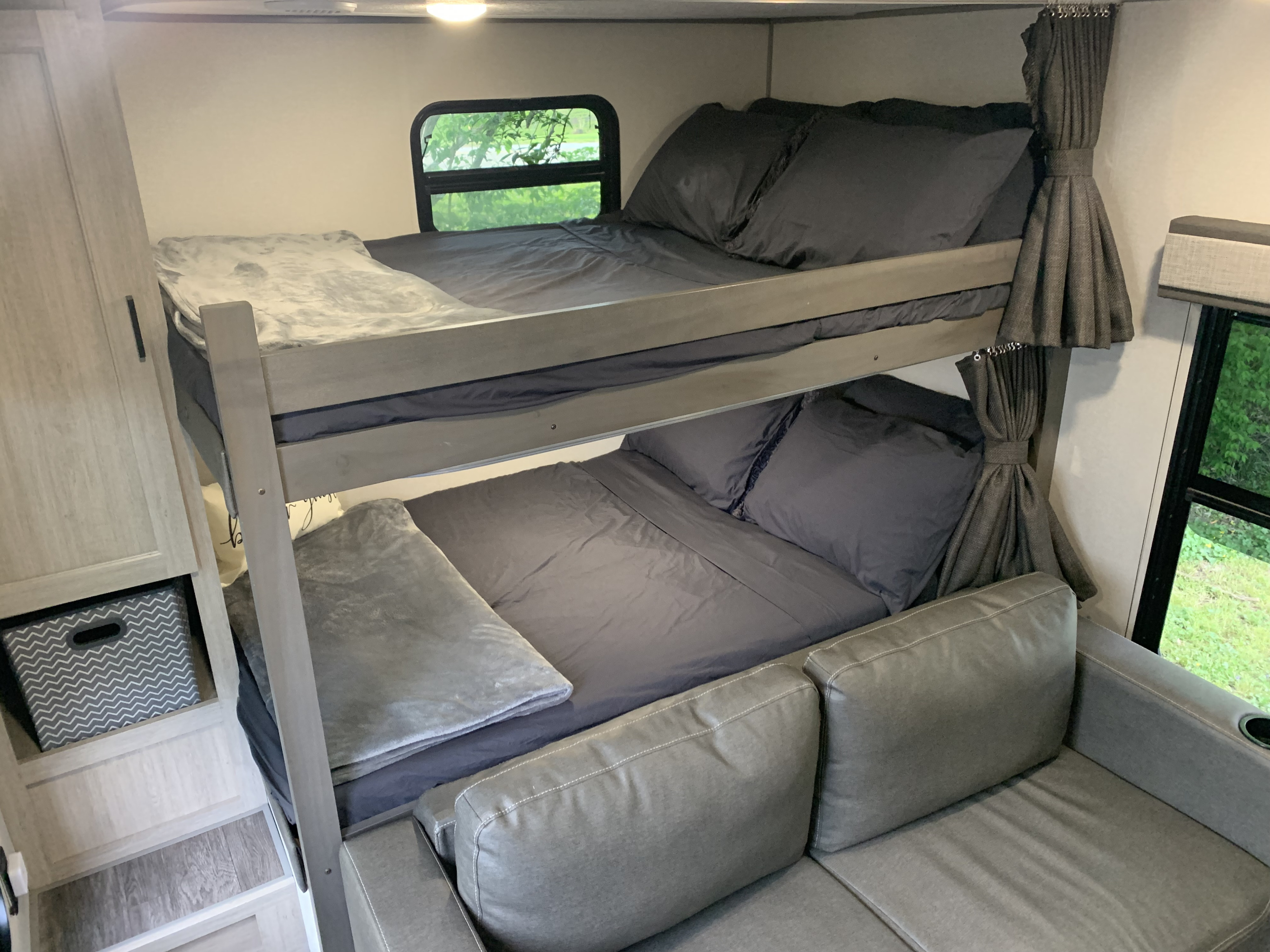 Cozy RV rental interior with gray bunk beds, a window showing greenery, a sofa, and storage. Perfect for family travel.. Forest River Aurora Aurora Light 2024