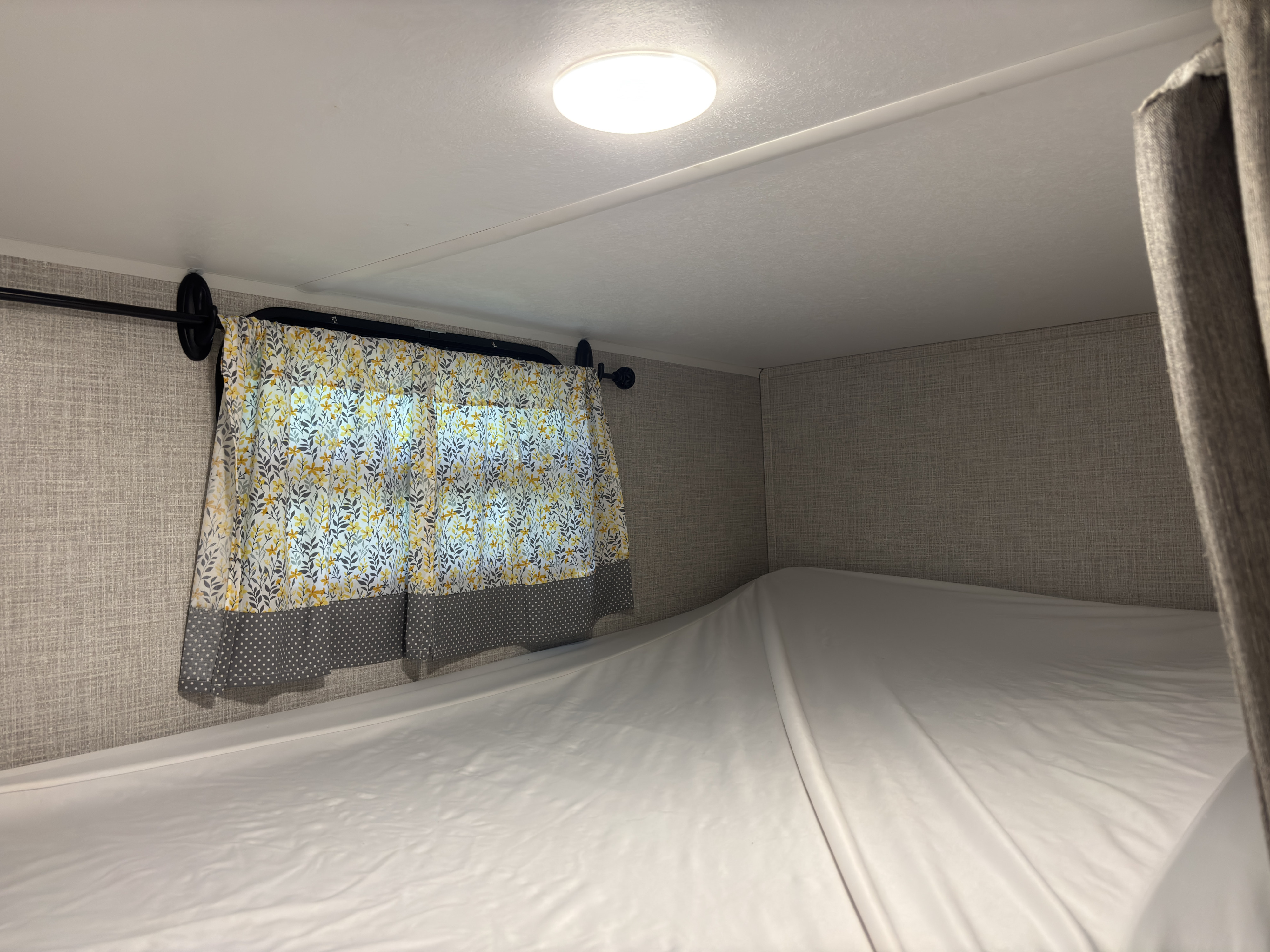 An RV rental's cozy bunk bed, complete with a bright floral curtain and textured walls, offers comfort for travel.. East to West Della Terra 2021