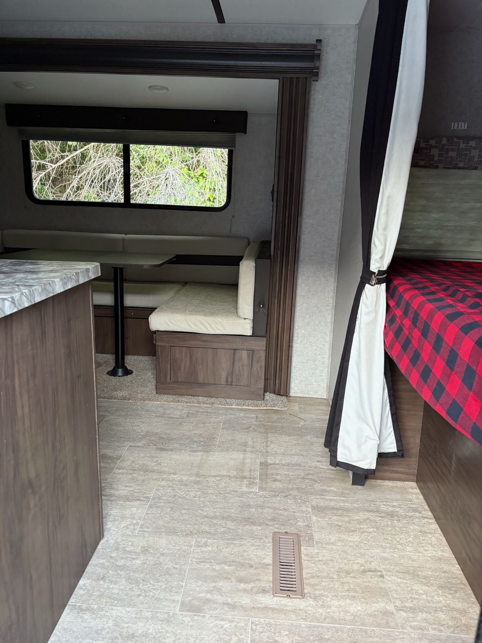 Cozy RV rental interior with a dinette, kitchenette counter, and bunk beds with a red plaid comforter.. Forest River Xlr Thunrderbolt 2020