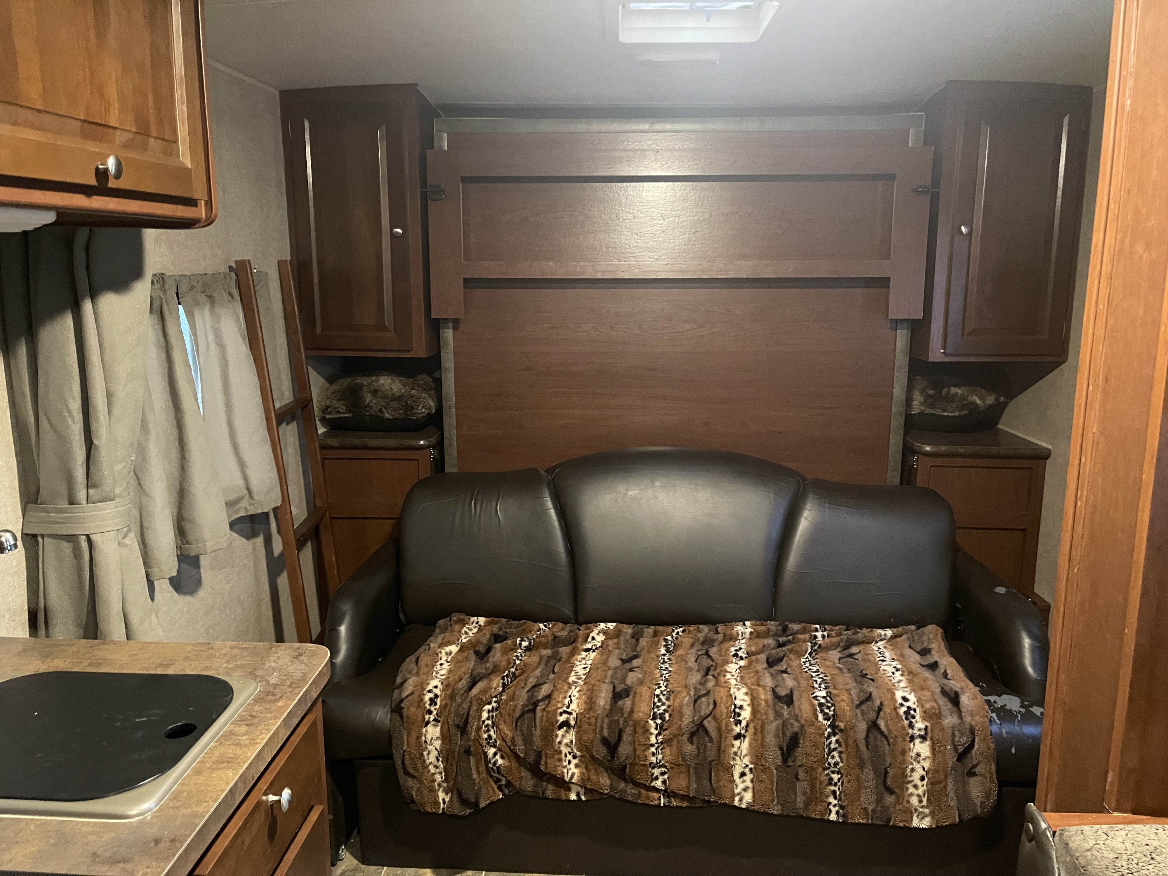 RV rental interior: a black couch with patterned blanket, wooden wall bed, and kitchen counter with sink cover.. Forest River Rockwood Mini Lite 2015