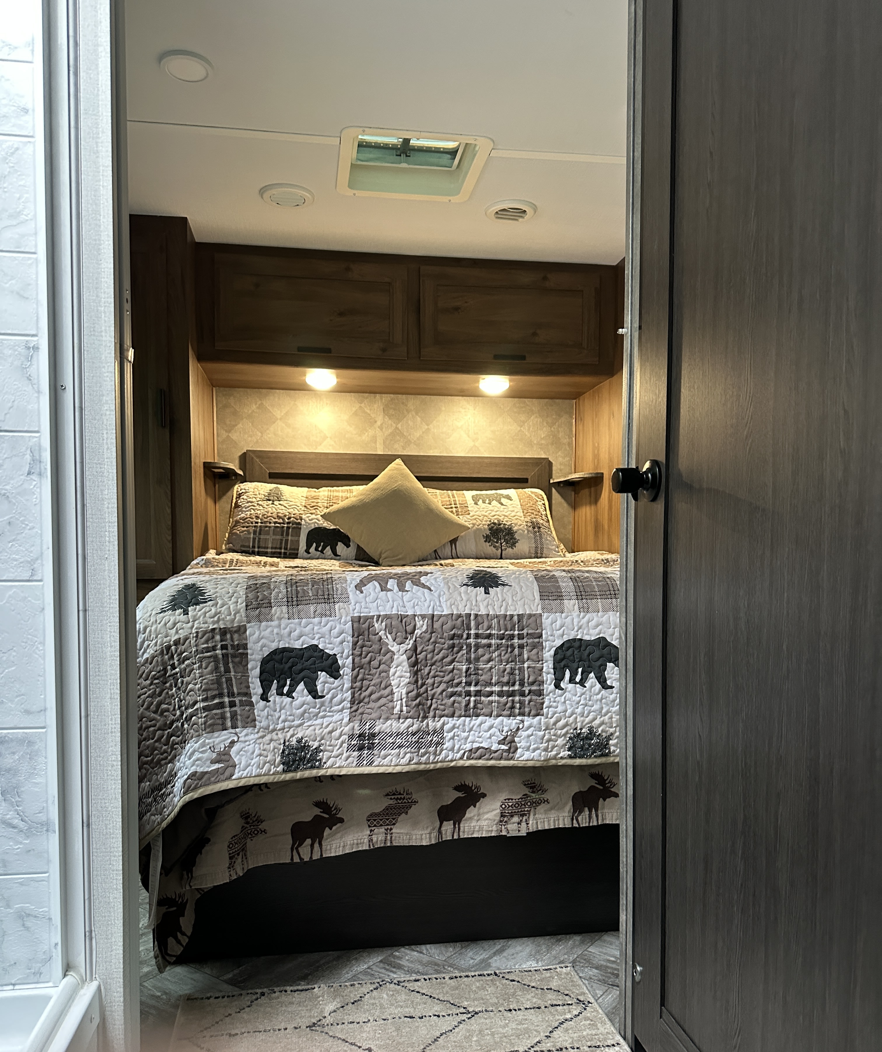Inviting RV rental bedroom with a rustic quilt featuring bears and deer, overhead lights, and storage. Ideal for cozy travels.. Forest River Sunseeker LE 2021