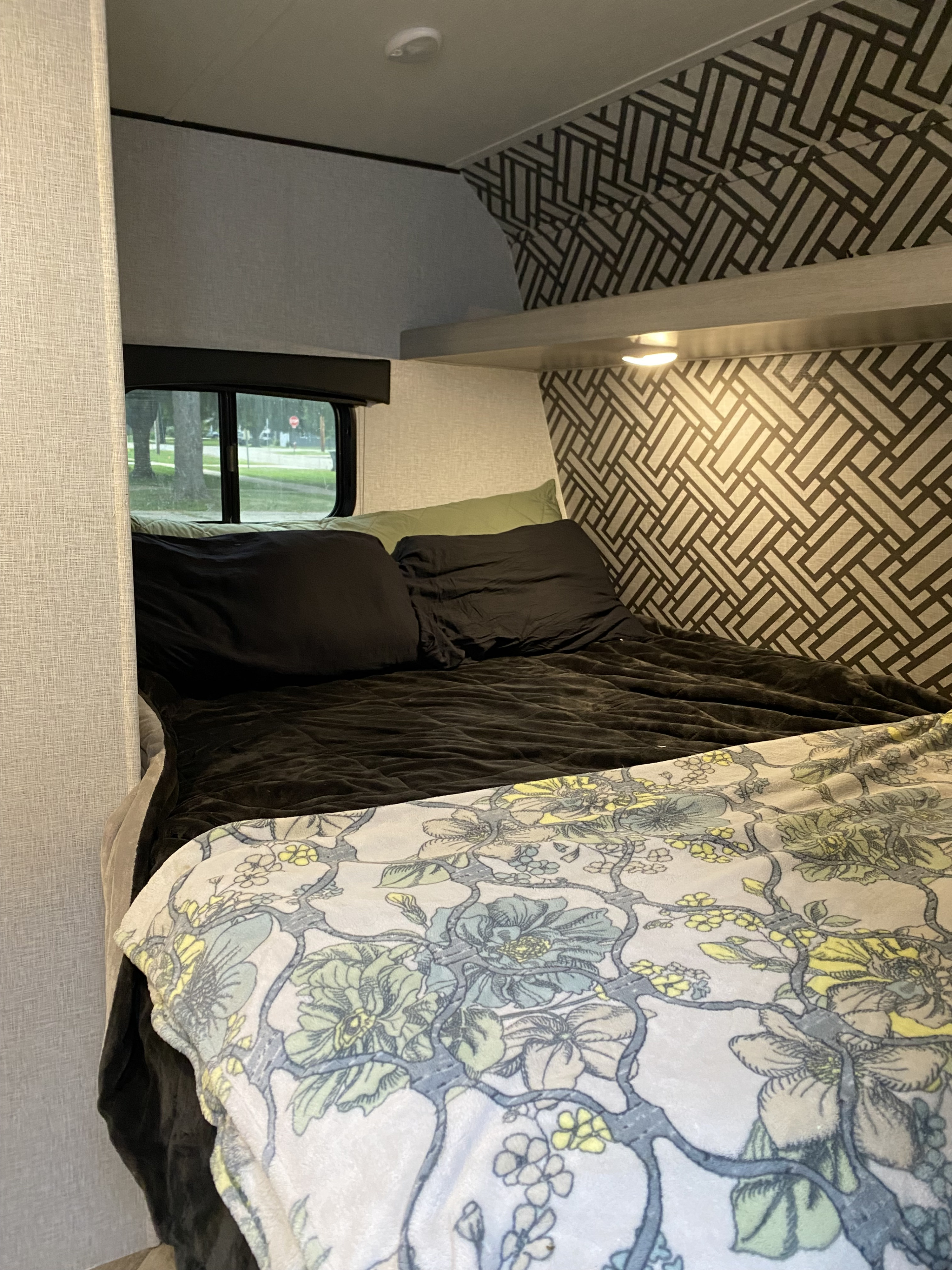 RV rental bedroom with a bed, black pillows, floral blanket, geometric patterned walls, and window view.. Crossroads RV Crossroads Zinger 18QB 2024