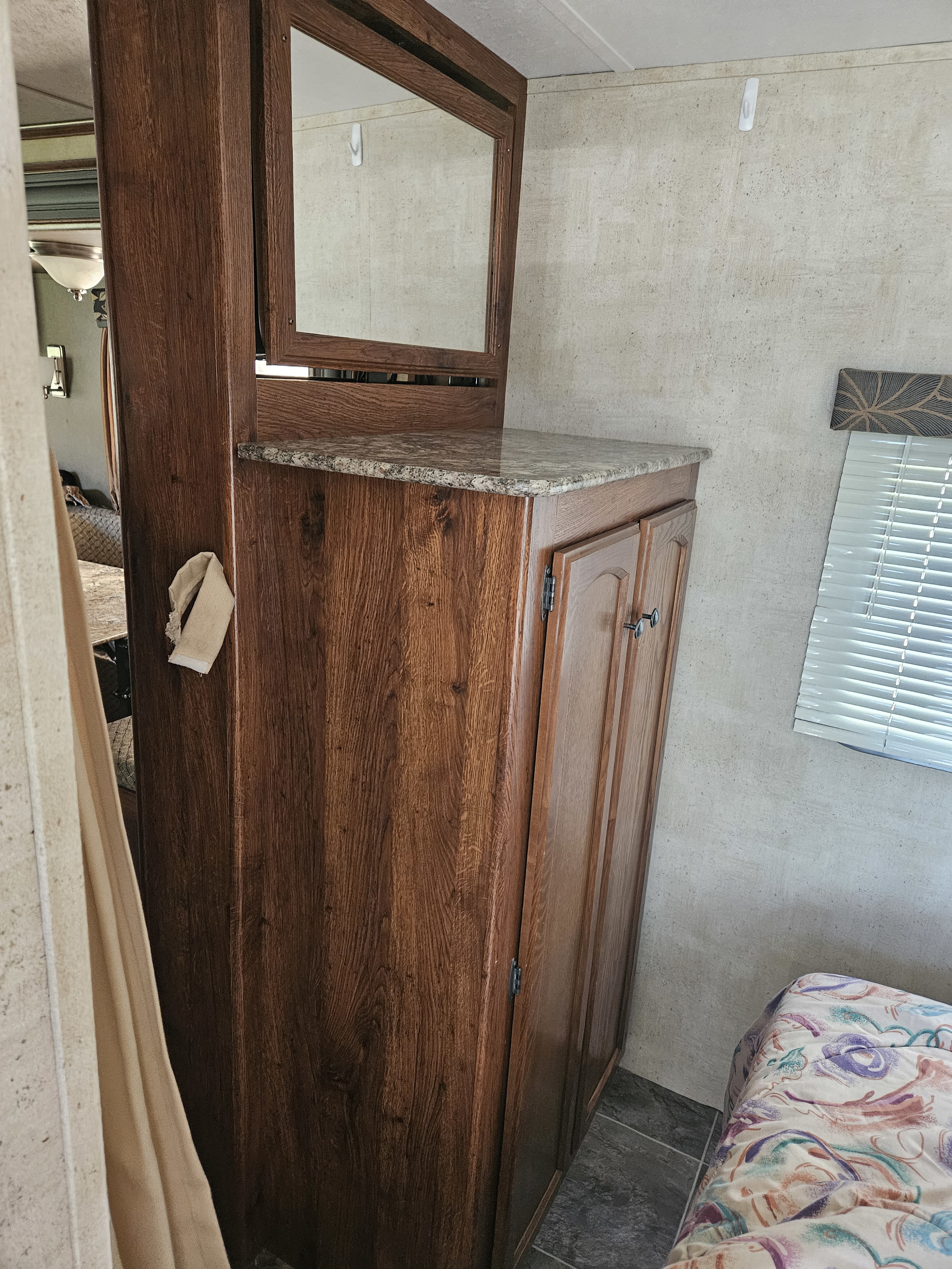 Cozy RV rental interior featuring a wood cabinet, granite-look counter, wall mirror, and part of a bed.. Keystone RV Hideout 2015