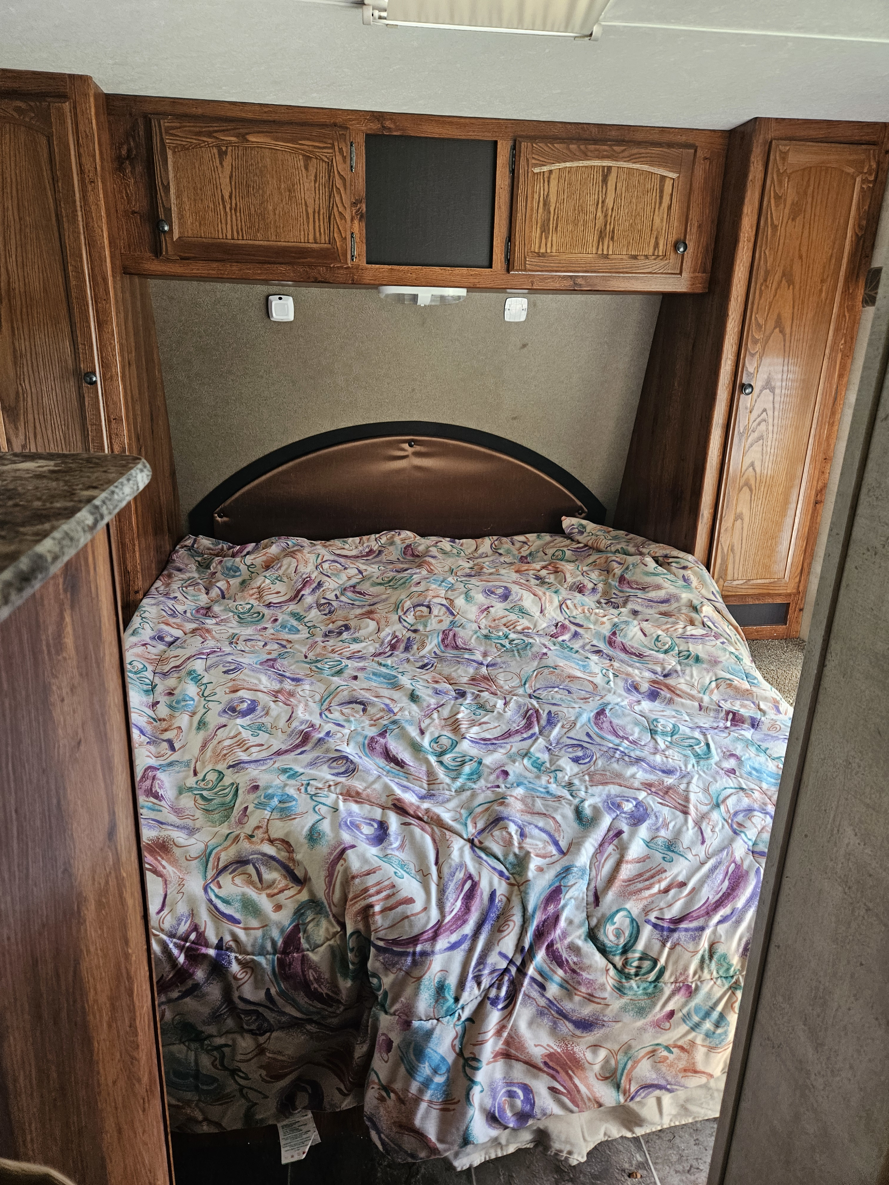 Cozy RV rental bedroom with a vibrant comforter, overhead cabinets, and side storage. Perfect for travel comfort.. Keystone RV Hideout 2015
