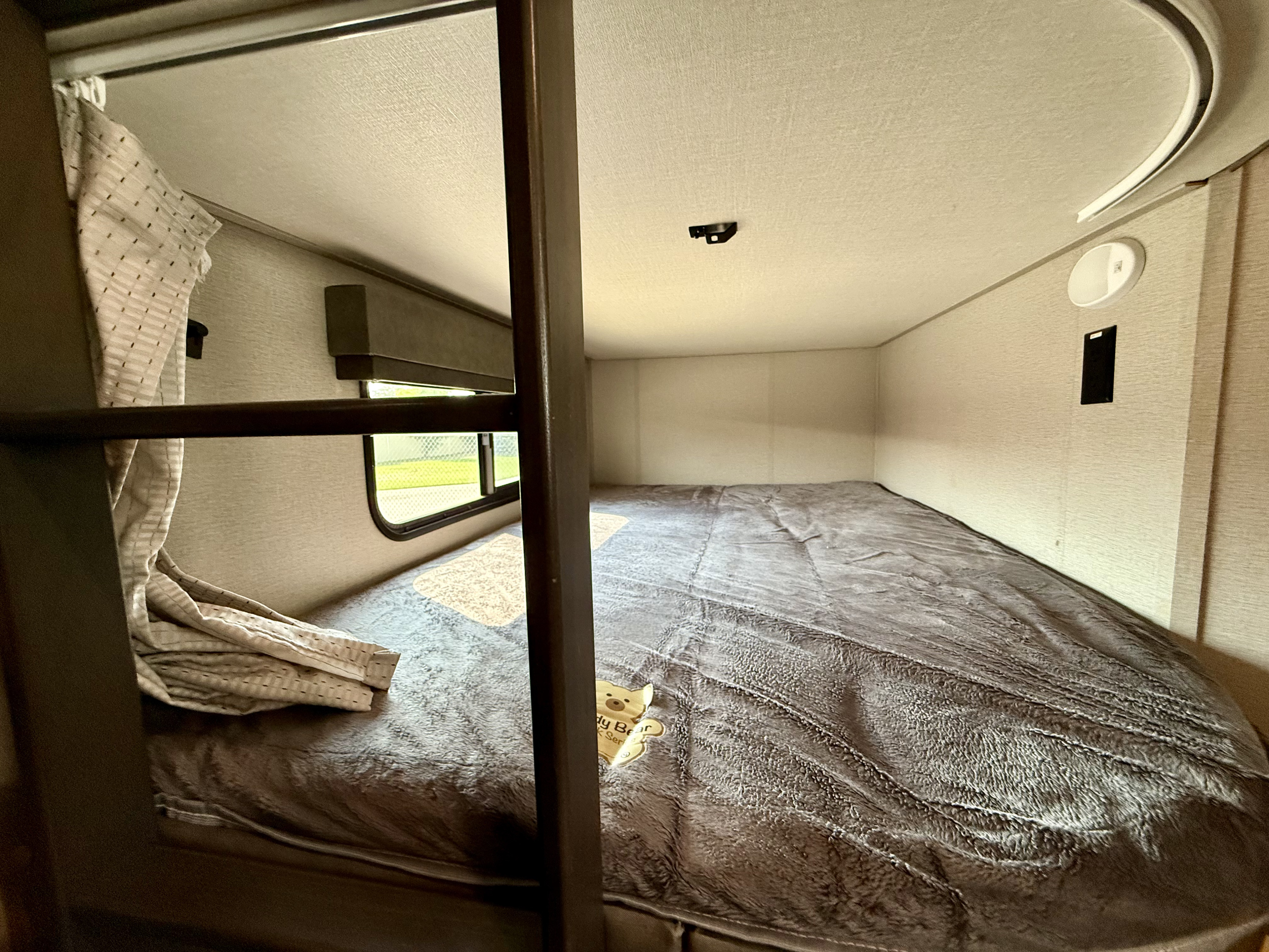 Cozy RV rental bunk bed with soft blanket and window view, ideal for travel.. Grand Design Imagine 2021