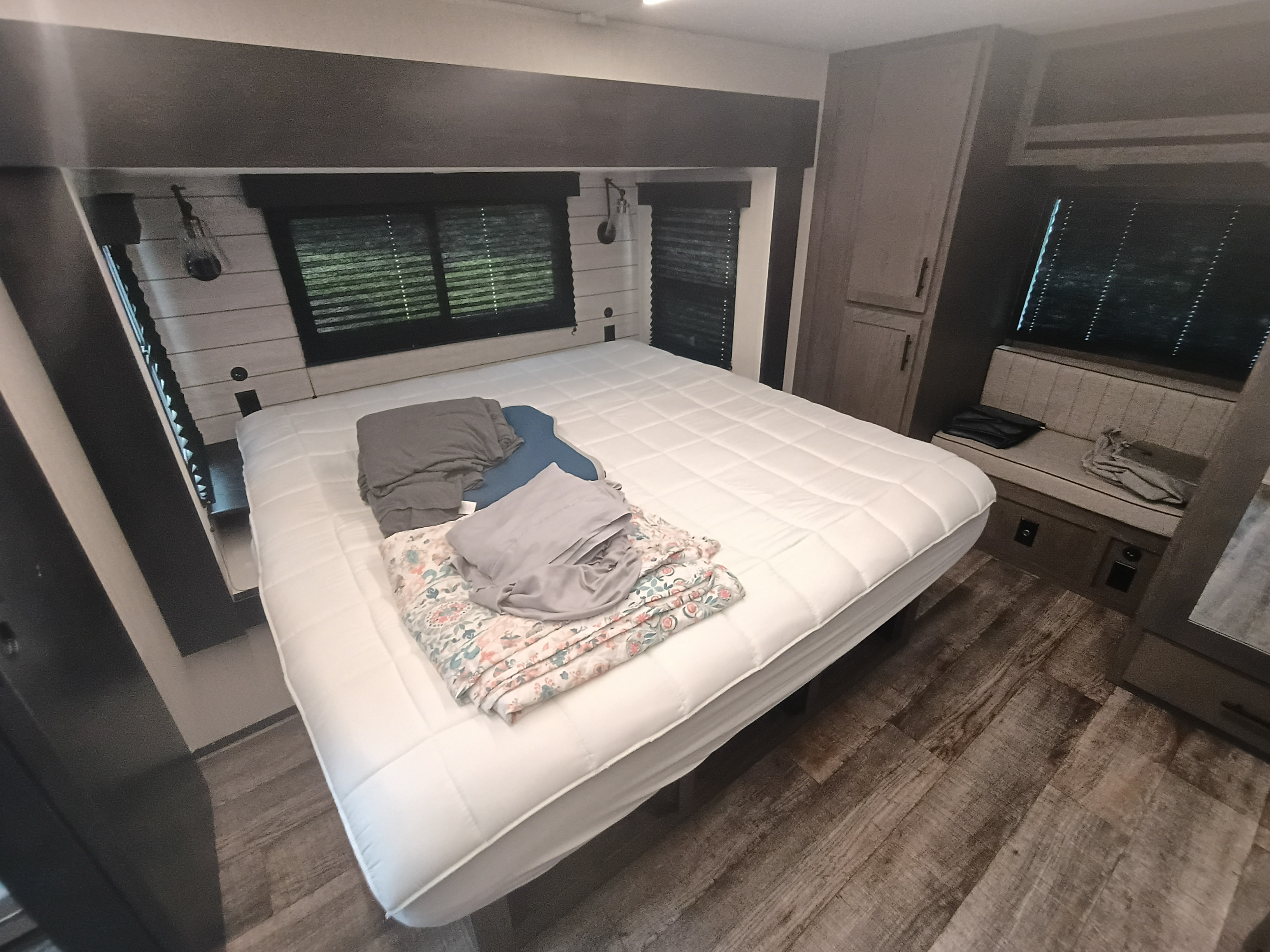 An RV rental bedroom with a white mattress, folded linens, window blinds, and built-in wood-look cabinets. Modern & functional.. Forest River Arctic Wolf 2025