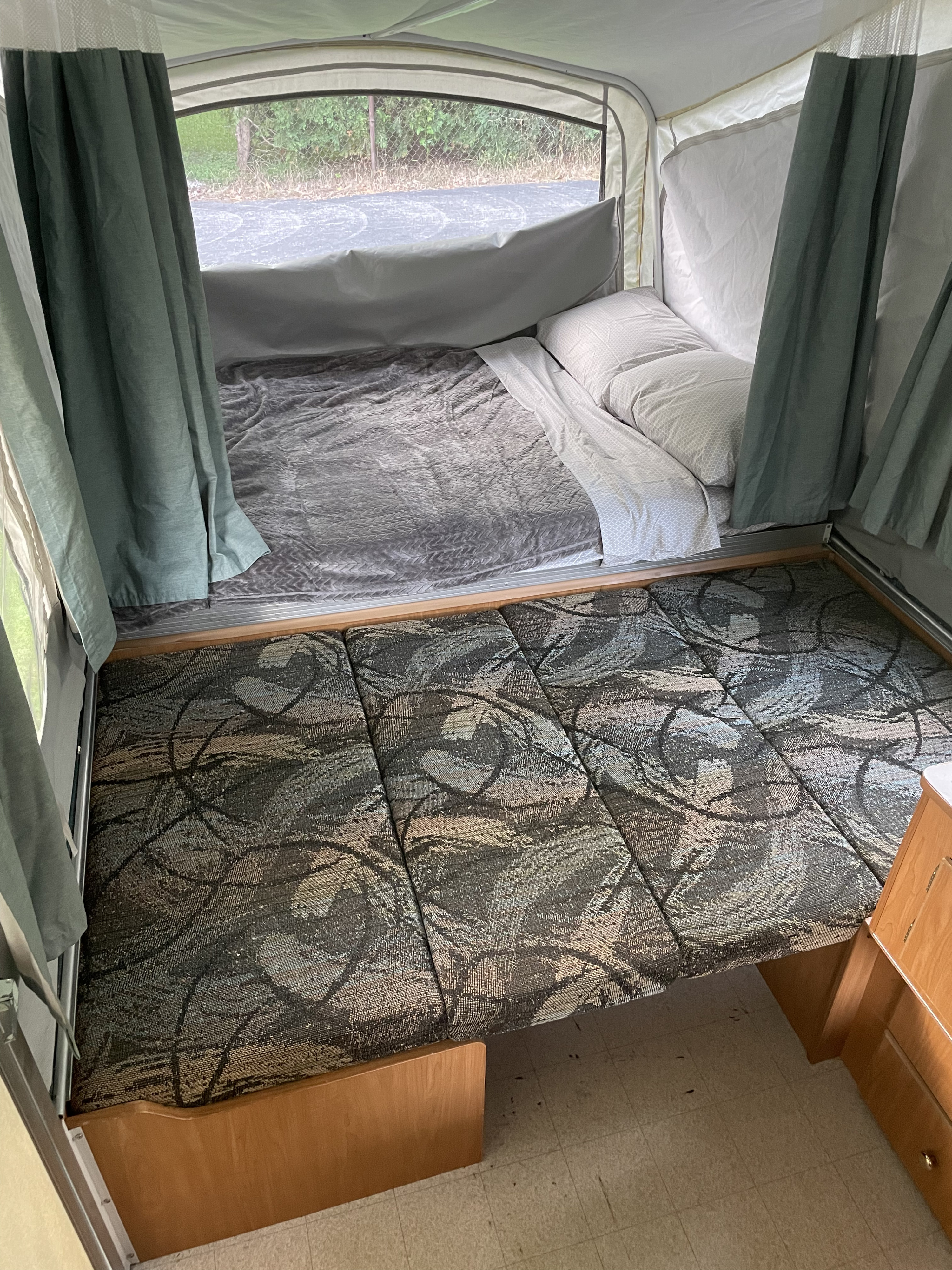 View inside an RV rental showing a comfortable bed, patterned cushions, and green privacy curtains.. Coleman Taos 2002