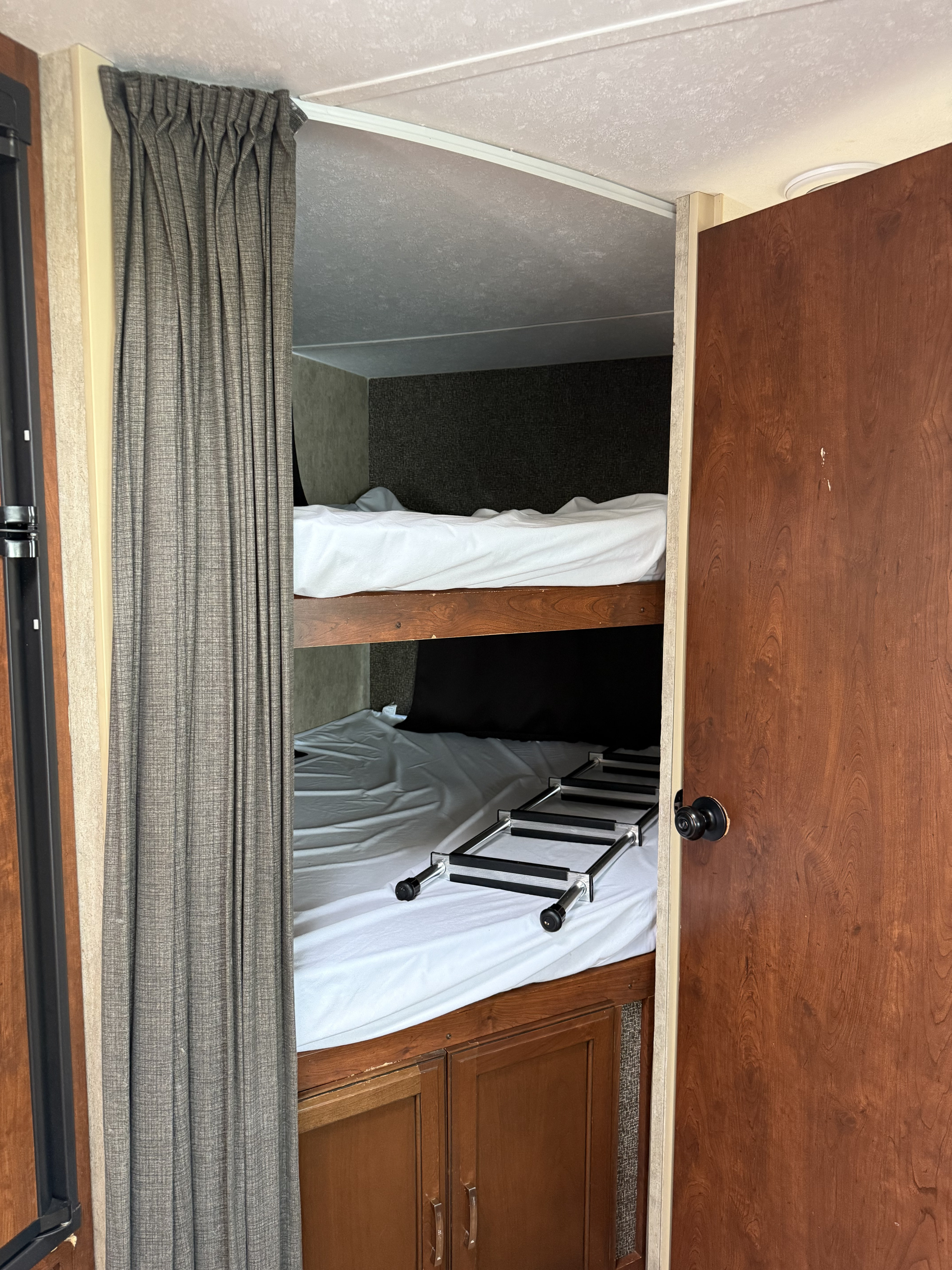 This RV rental features a cozy bunk bed sleeping area with white bedding and a ladder, behind a privacy curtain.. Keystone Passport 2016