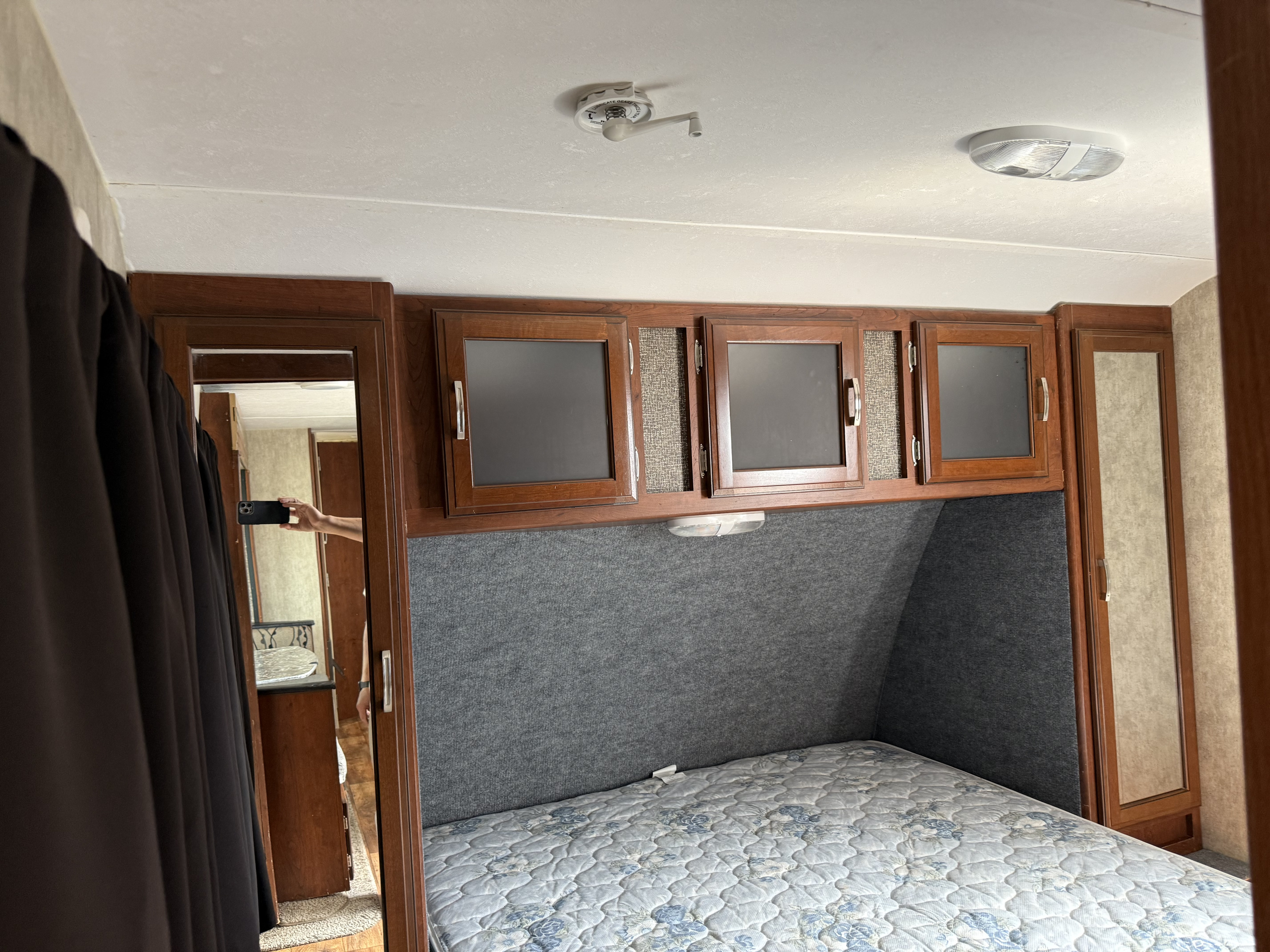 RV rental bedroom with a comfortable bed, overhead cabinets, and soft gray wall panels, showing a cozy RV interior.. Keystone Passport 2016