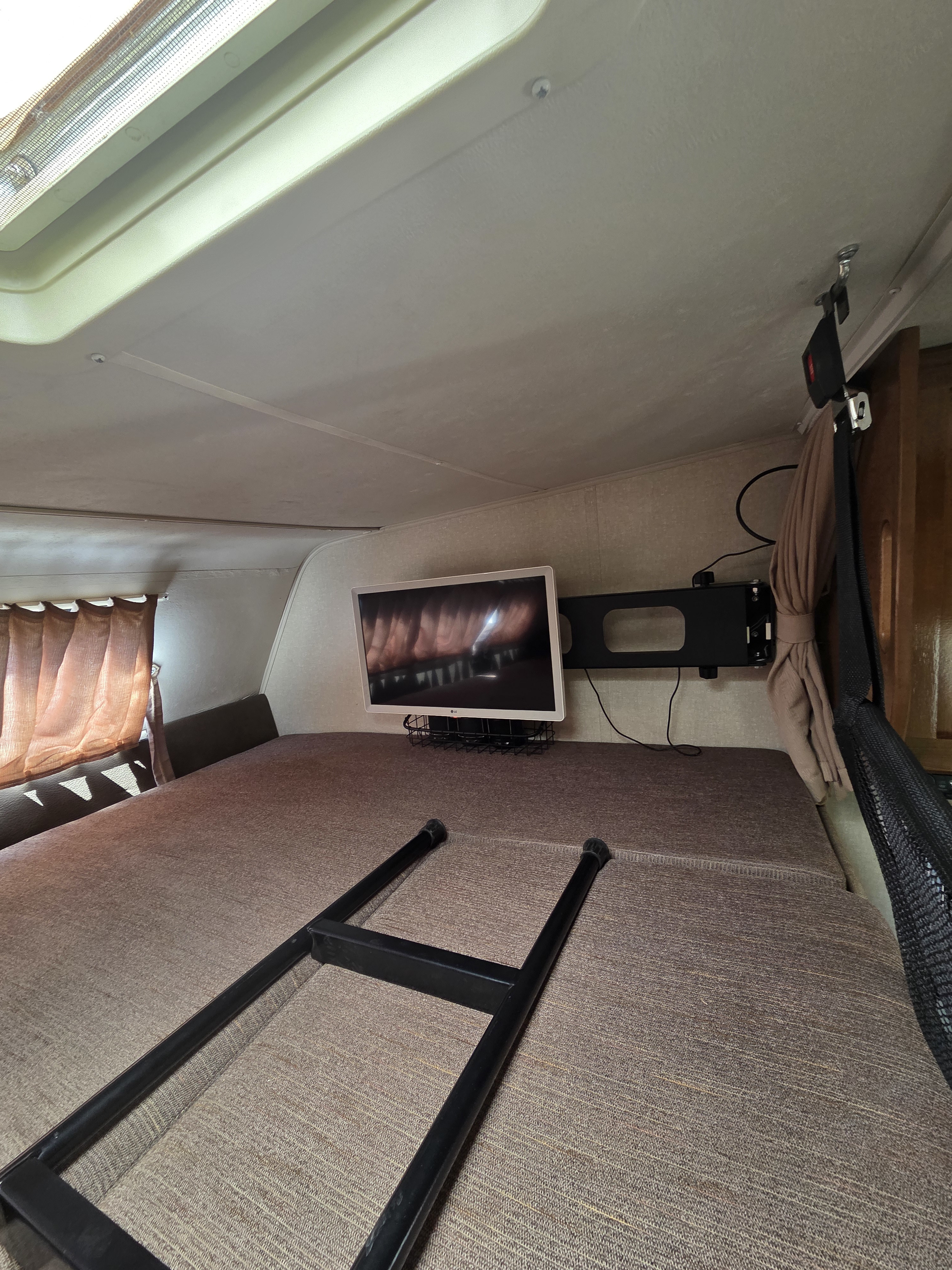 Inside an RV rental: cozy sleeping area with a mounted TV, access ladder, and ceiling skylight.. Forest River Coachmen Leprechaun 2019