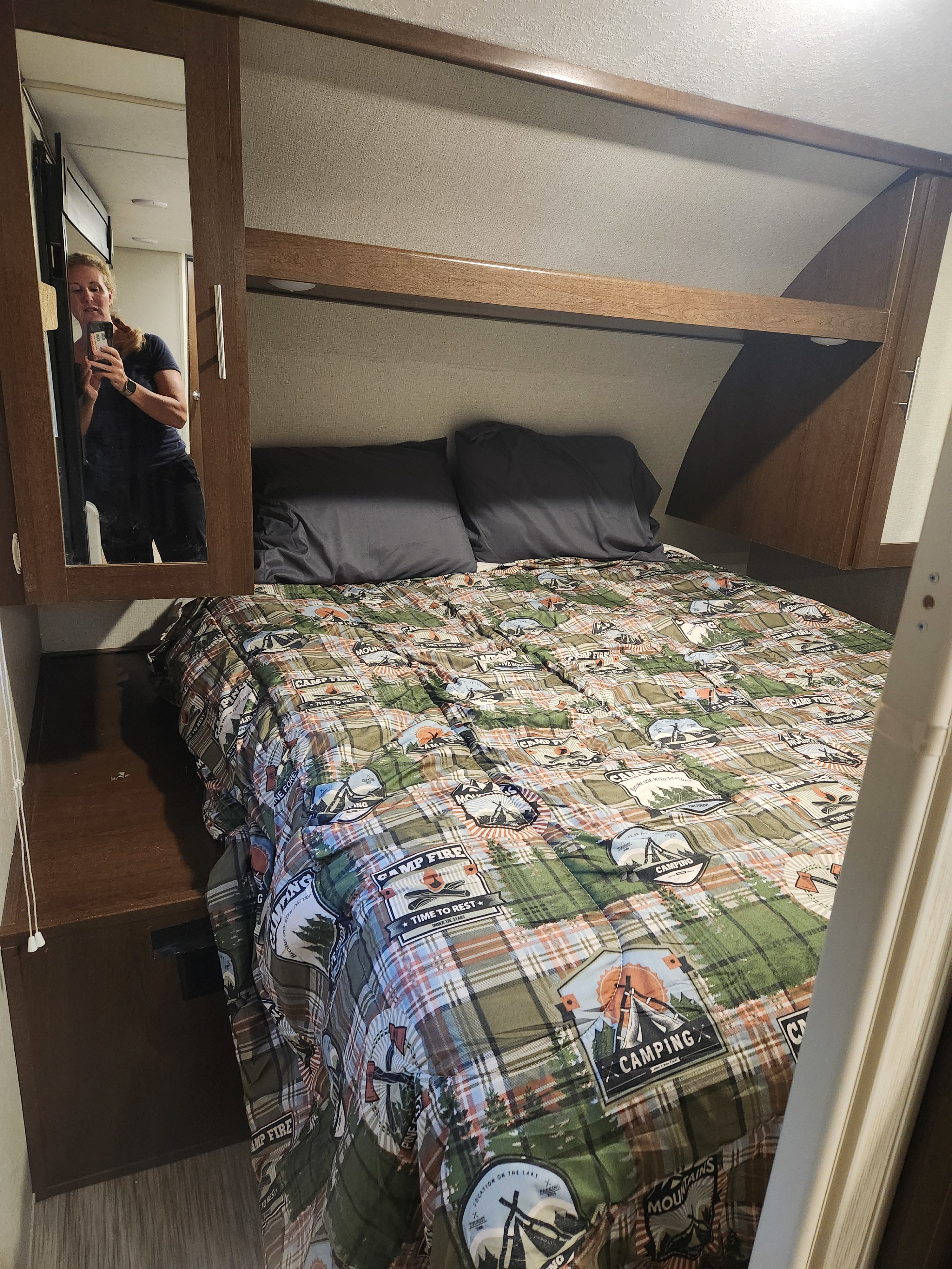 Cozy RV rental bedroom featuring a plaid camping comforter, dark pillows, and a mirrored cabinet. Ideal for adventurers.. Forest River Acadia 2018