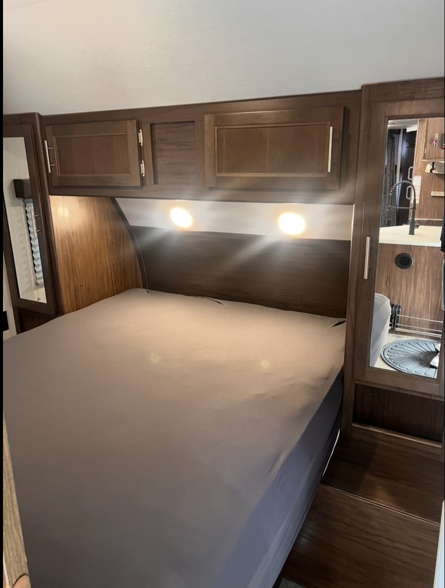 Experience comfort in this rv rental bedroom: queen bed, dark wood cabinets, and bright task lighting.. Forest River Cherokee Grey Wolf 2019