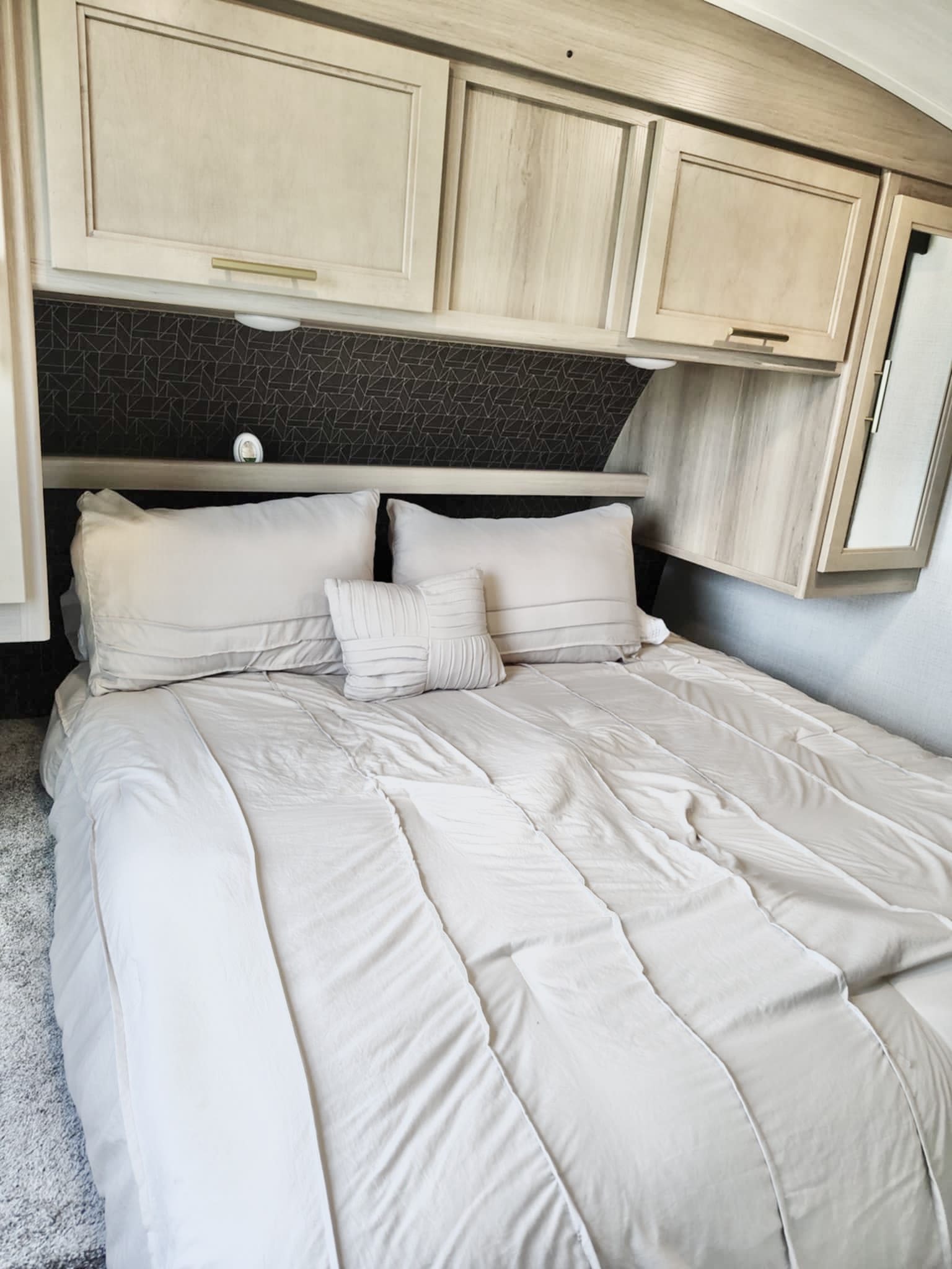 Cozy RV rental bedroom features a comfy bed with light sheets, plush pillows, and smart overhead storage.. Keystone RV Outback Ultra Lite 2024