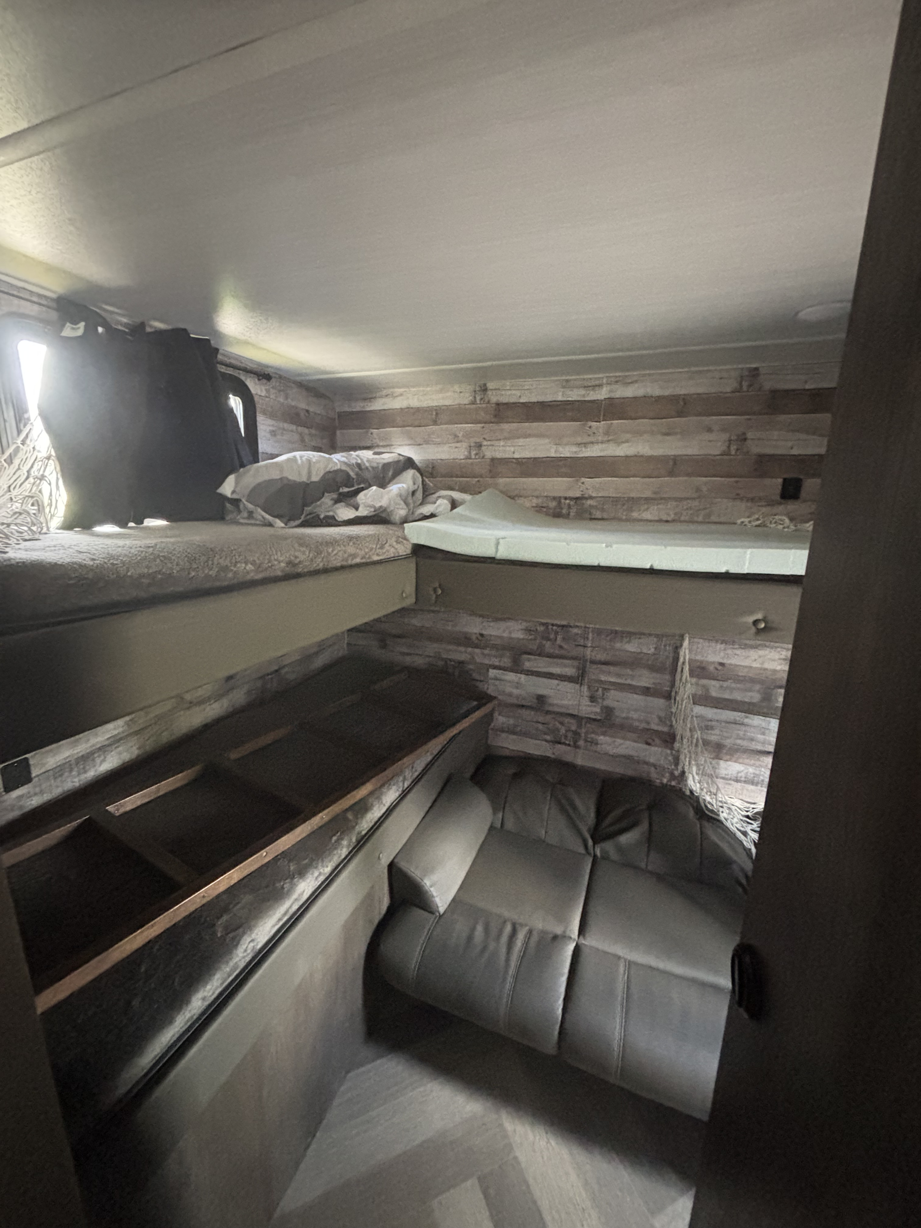 Interior of an RV rental: a cozy space with two bunk beds above a comfortable sofa, and rustic wood-paneled walls.. Forest River Salem Cruise Lite 2021