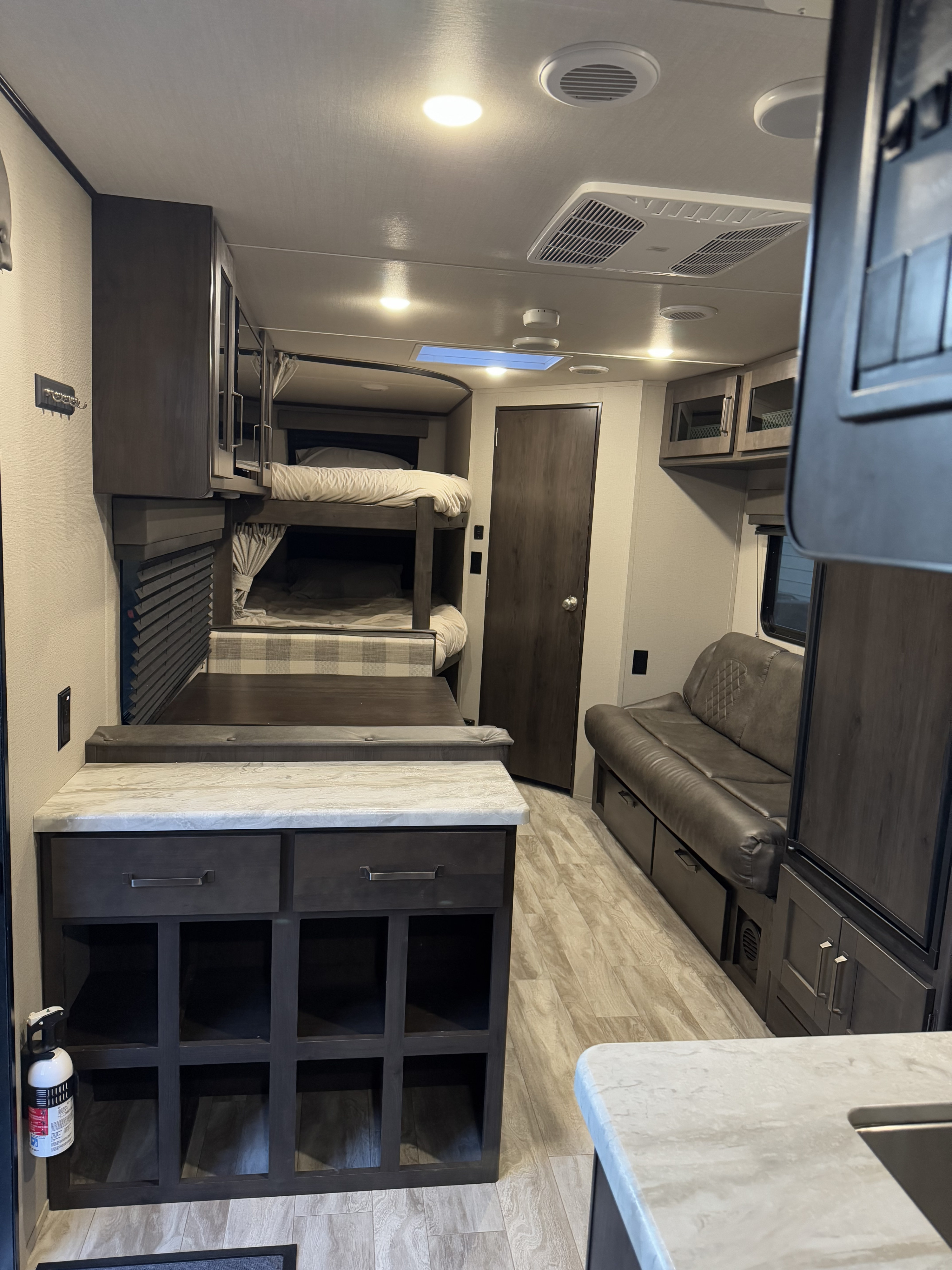 Inside an RV rental, showing bunk beds, a seating area, and a kitchen island.. Grand Design Transcend Xplor 2021