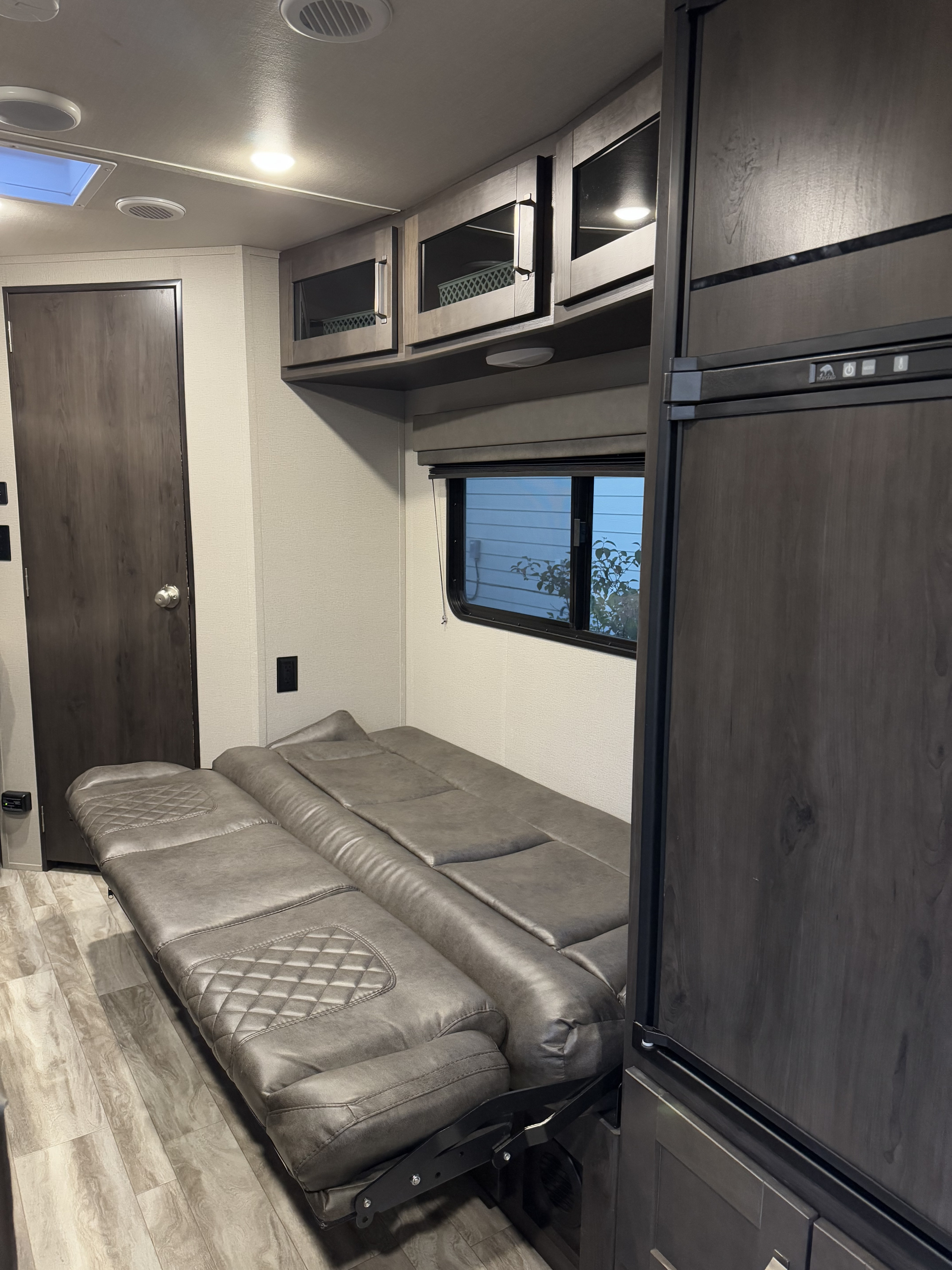 RV rental: The interior features a versatile gray fold-out sofa bed, dark refrigerator, and overhead cabinets with a window.. Grand Design Transcend Xplor 2021