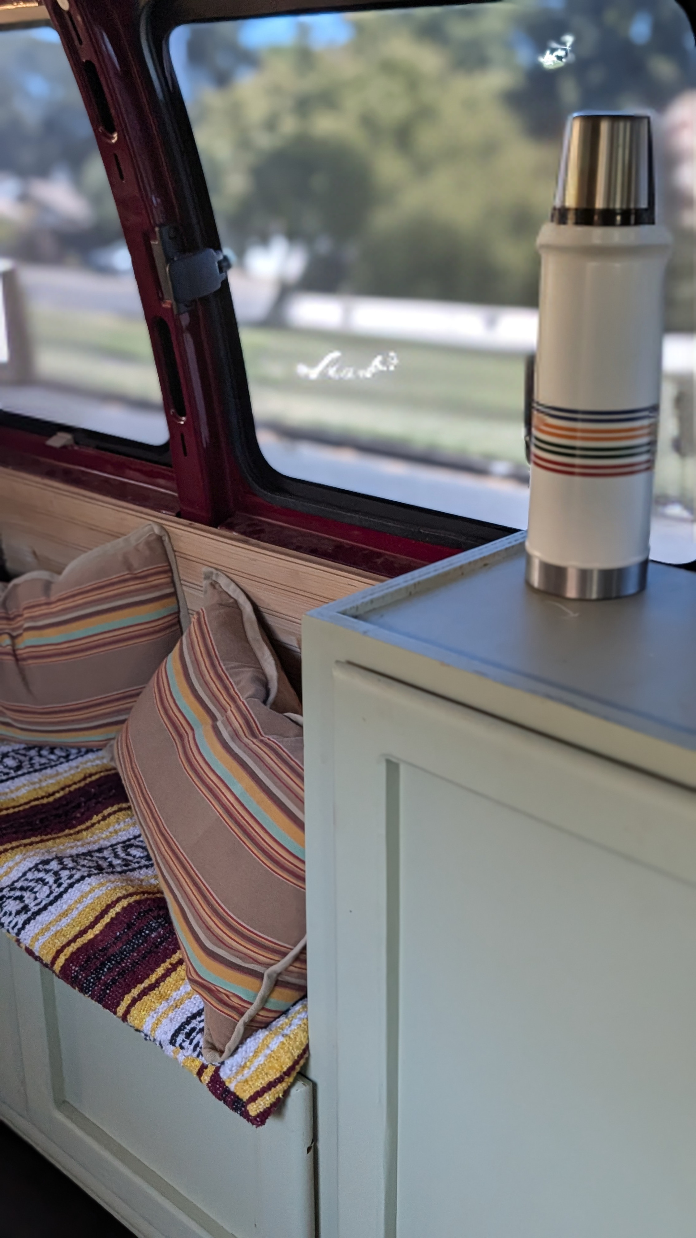 Inside an RV rental: a cozy bench with striped pillows, a patterned blanket, and a thermos on a cabinet next to the window.. Chevrolet Express 3500 2007