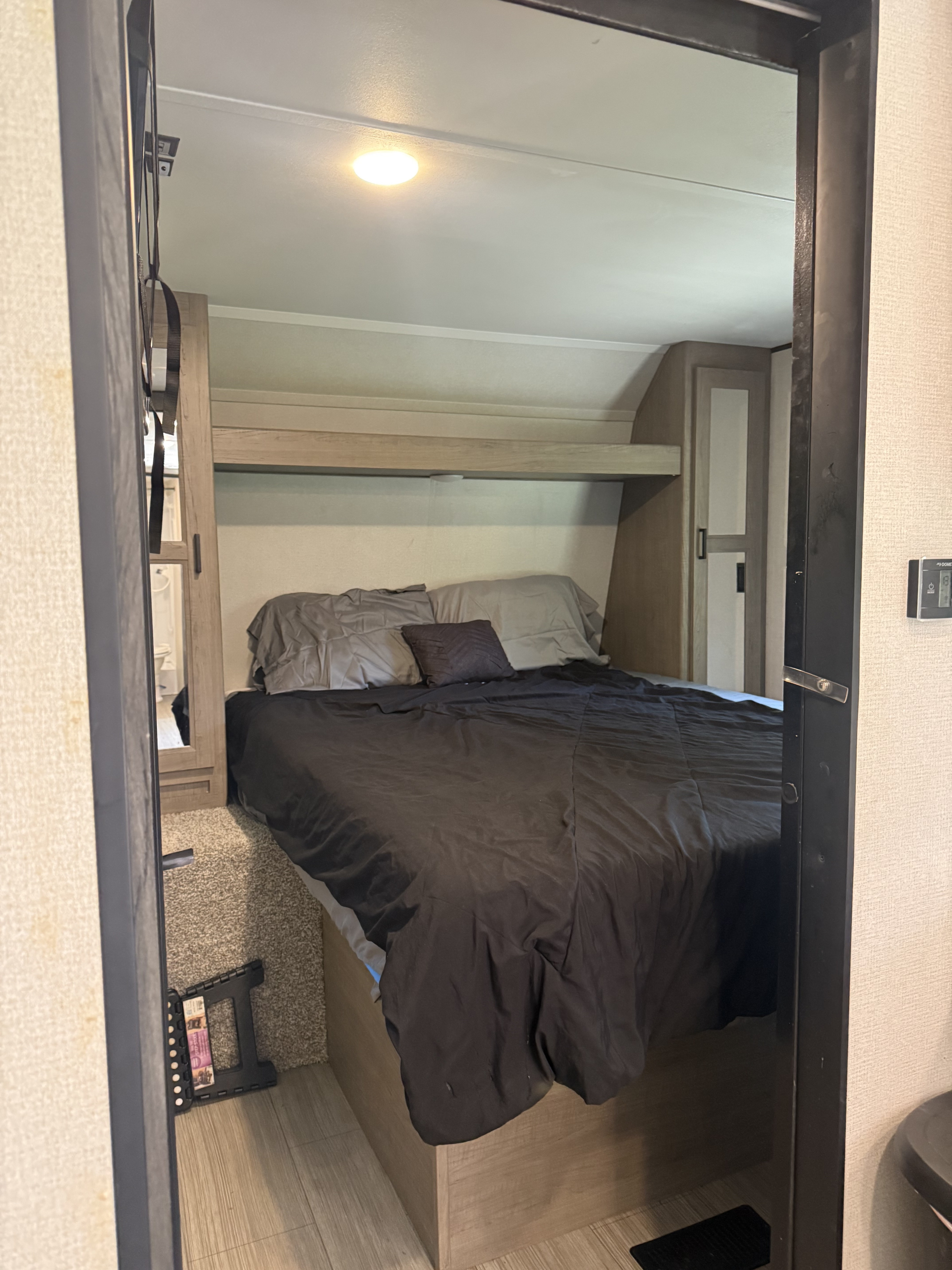 Inside an RV rental bedroom: a bed with dark bedding, built-in storage, and a mirrored door, showcasing the compact interior.. Keystone Hideout 250 BH 2021