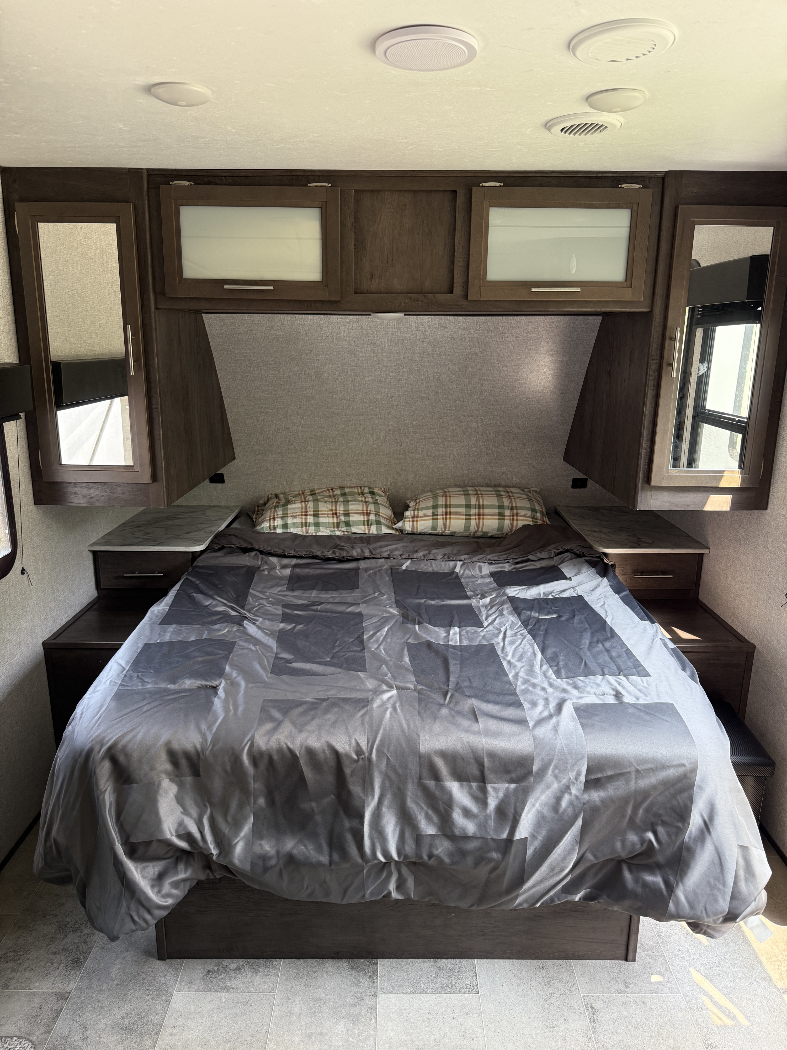 Spacious RV rental bedroom featuring a large bed with plaid pillows, dark wood cabinets, and modern ceiling features.. Dutchmen Coleman Light 2020