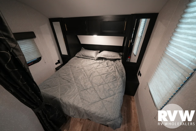 An RV rental bedroom features a comfy bed with grey comforter, dark built-in cabinets, and bright windows, ready for your trip.. Forest River Cherokee Grey Wolf 2022