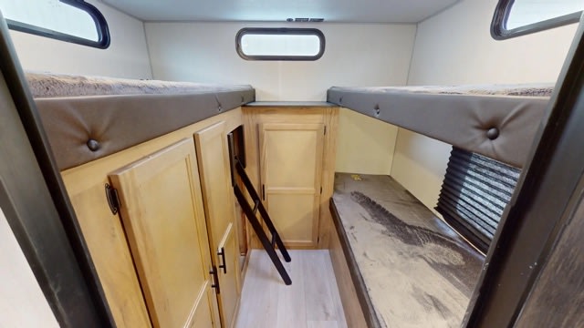 Spacious RV rental bunkhouse: two upper bunks, a lower bed, storage cabinets, and an access ladder are visible.. Forest River Cherokee Grey Wolf 2022