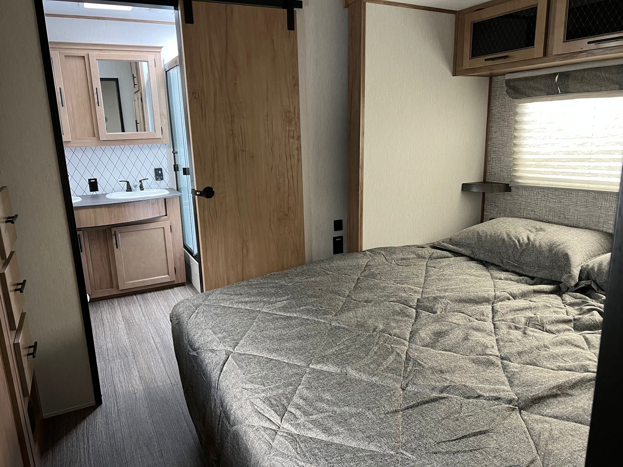 RV rental's modern interior: cozy bedroom with gray bedding, offering a view into the bright bathroom vanity.. Forest River Sabre 2023