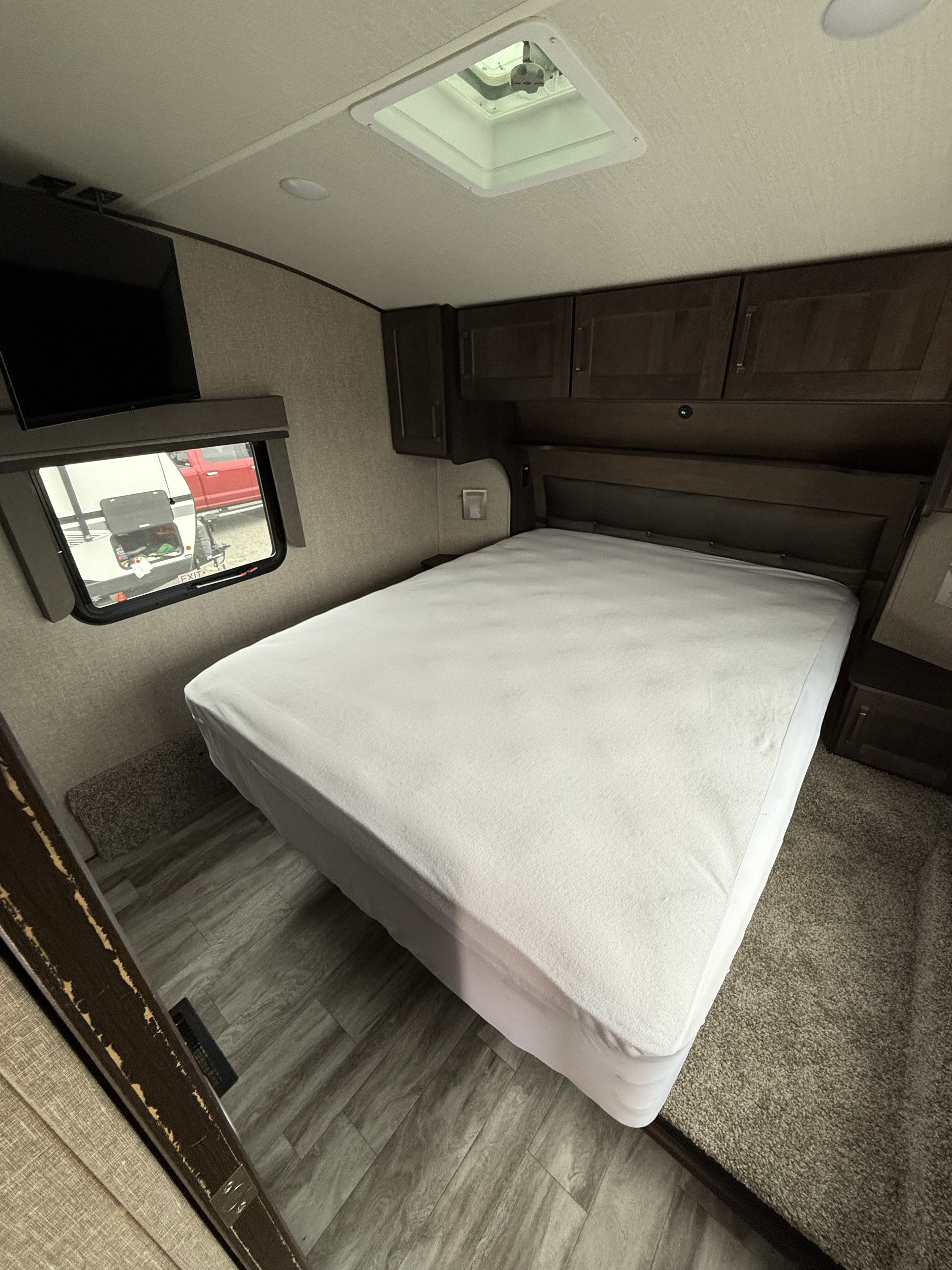 RV rental bedroom showcasing a bed with white cover, TV, overhead cabinets, and window with outdoor view.. Grand Design Reflection 2022