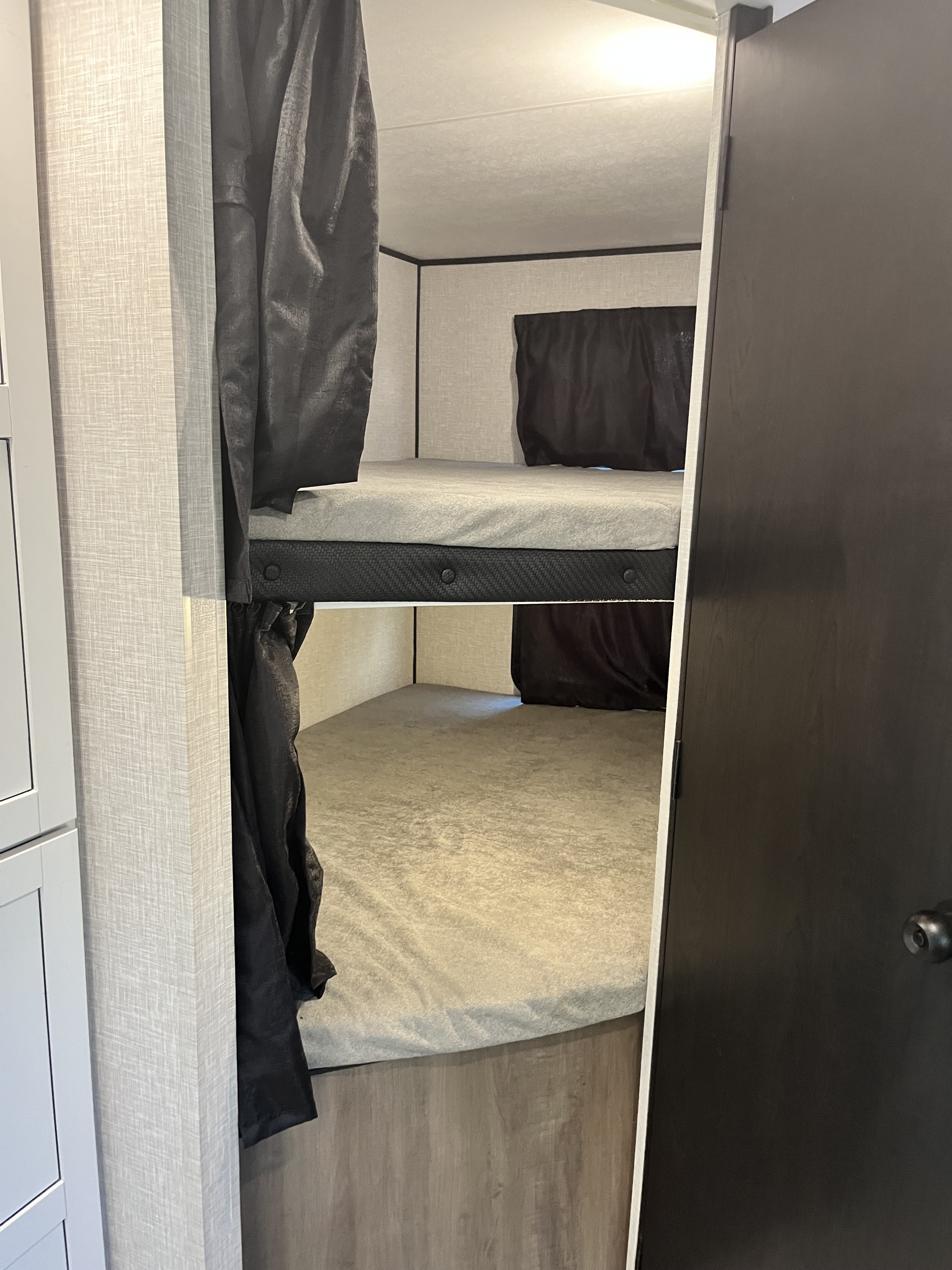 Comfortable bunk beds with privacy curtains inside an RV rental, ideal for family travel and cozy nights.. 58TBP0BPXS77L3080 Go Play 2025