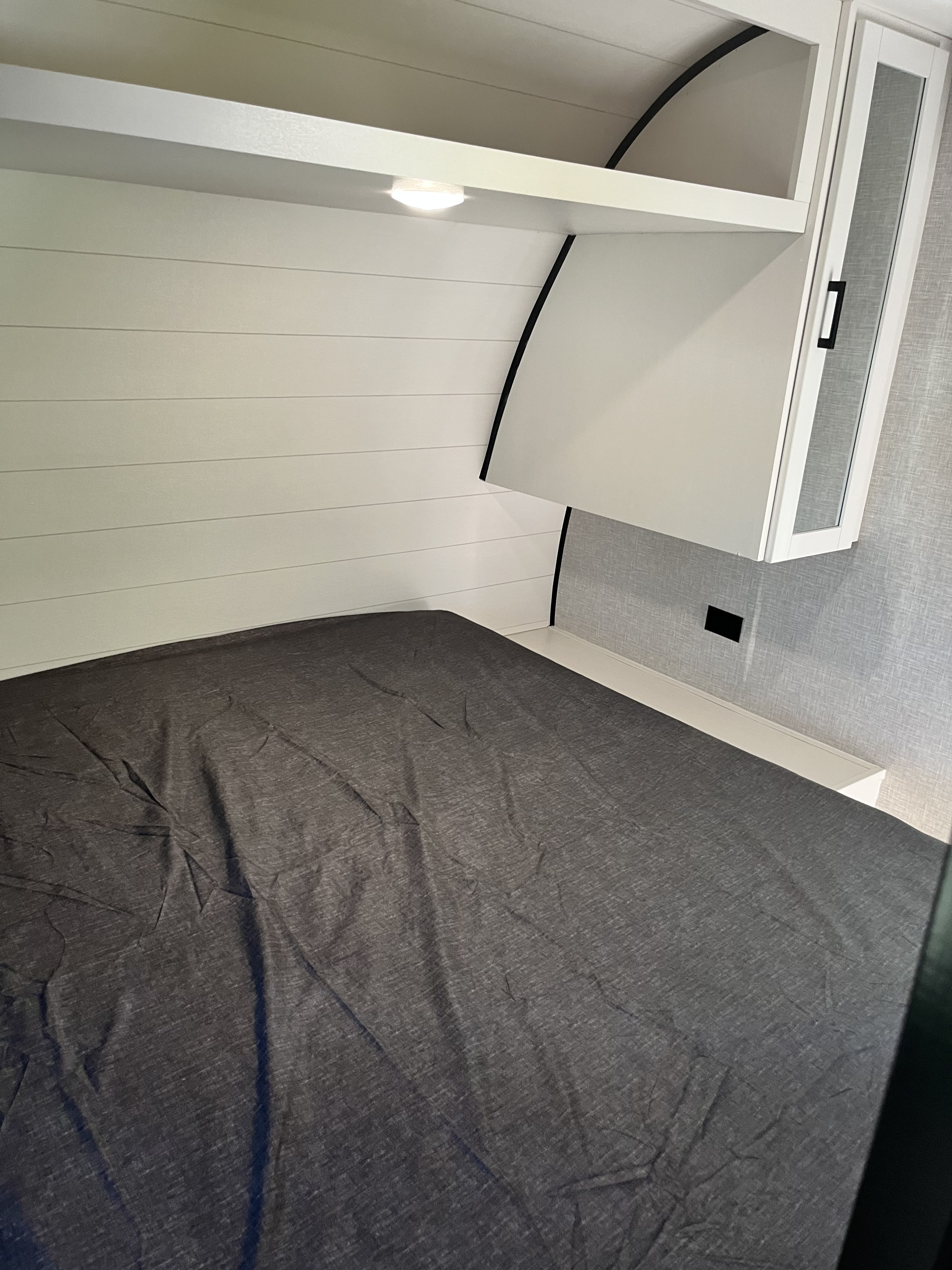 Cozy RV rental bedroom: dark gray bed, white shiplap walls, overhead storage with light, and bedside cabinet.. 58TBP0BPXS77L3080 Go Play 2025