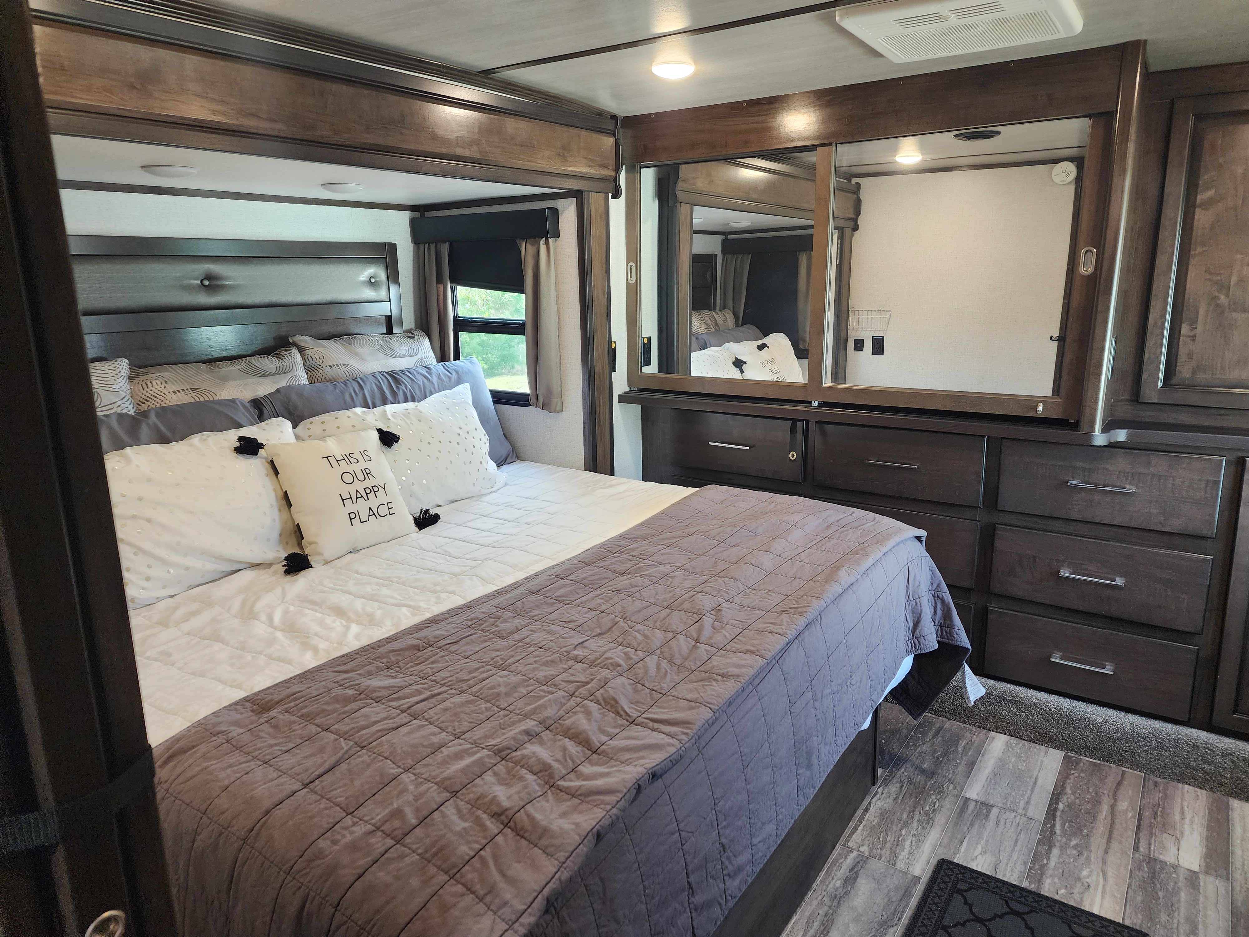 Comfortable RV rental bedroom with a large bed, dark wood storage, mirrored wardrobe, and a large window.. Dutchmen Yukon 2021