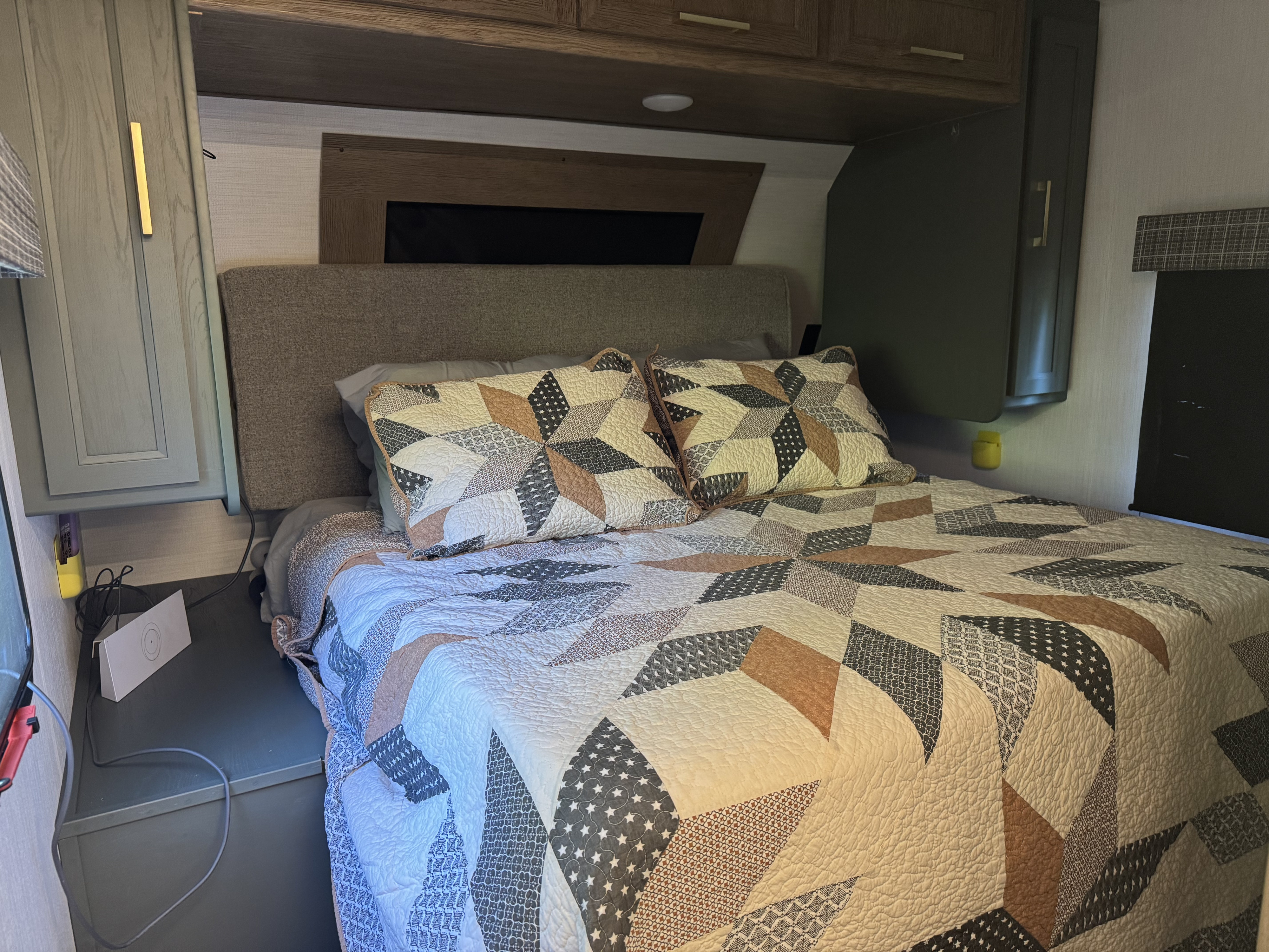 Cozy RV rental bedroom features a patterned quilt, headboard, and compact storage for a comfortable travel experience.. Heartland RVs Eddie Bauer 2024