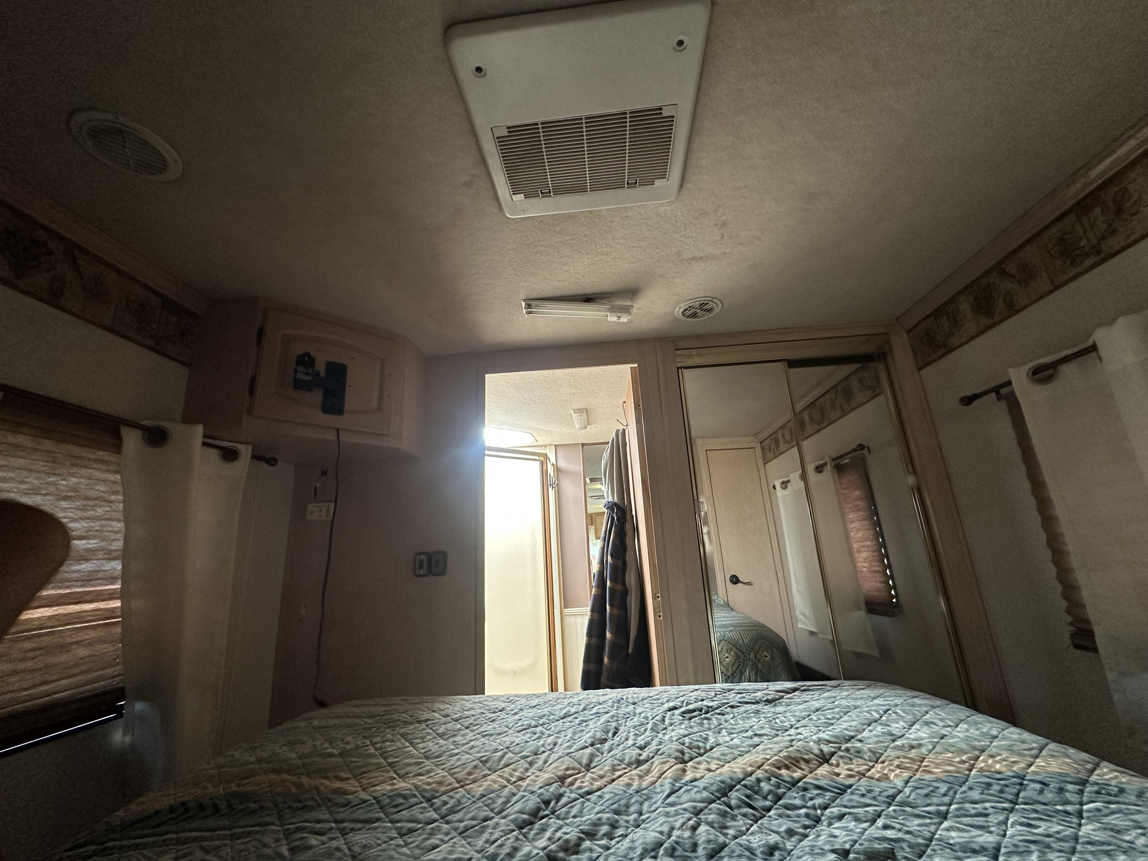 Spacious RV rental bedroom featuring a quilted bed, mirrored closet, ceiling AC unit, and privacy blinds.. Coachmen Santara 2000