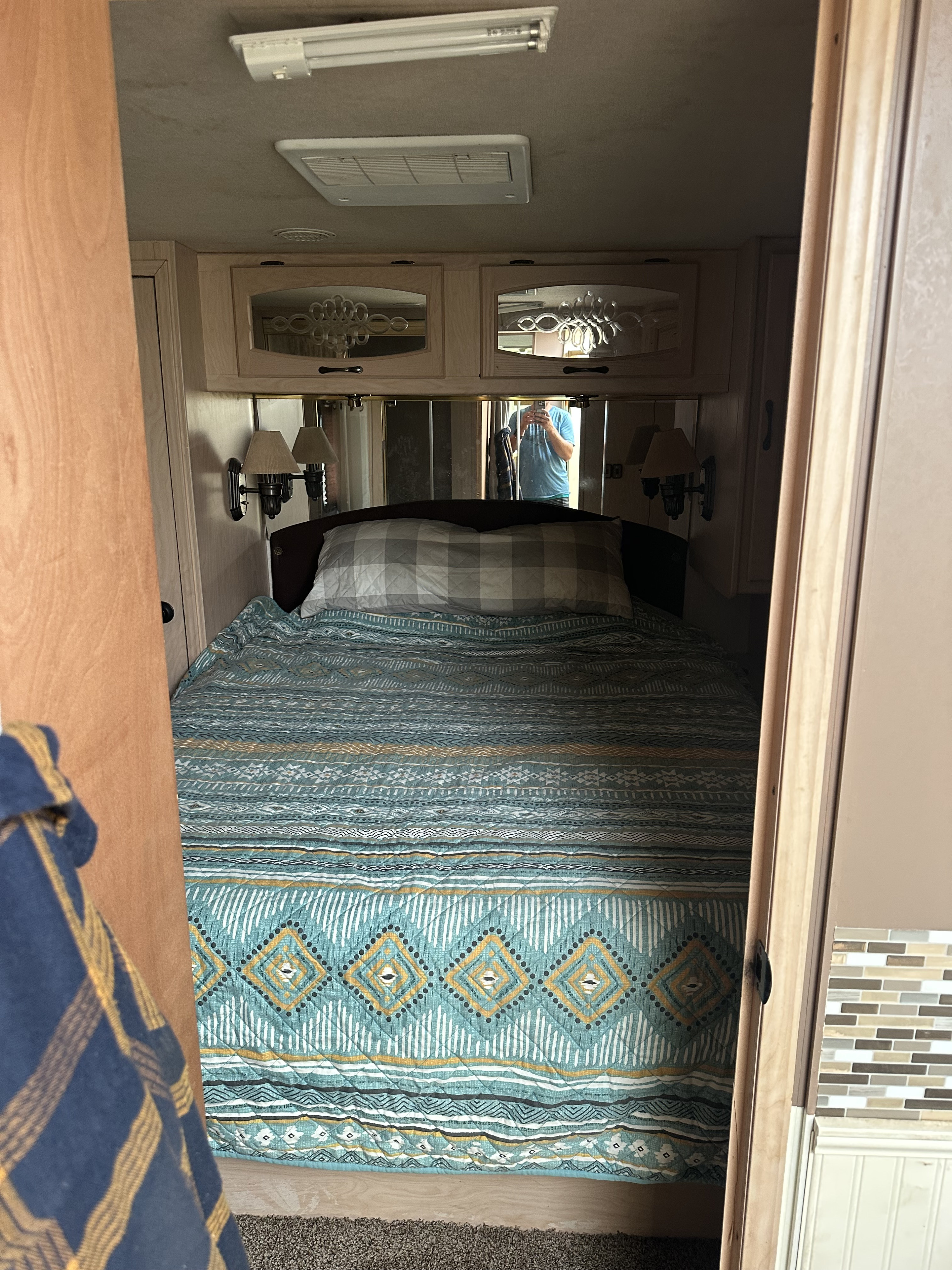 Step inside this RV rental bedroom featuring a comfy bed with a vibrant teal comforter, practical overhead storage, and reading lamps.. Coachmen Santara 2000