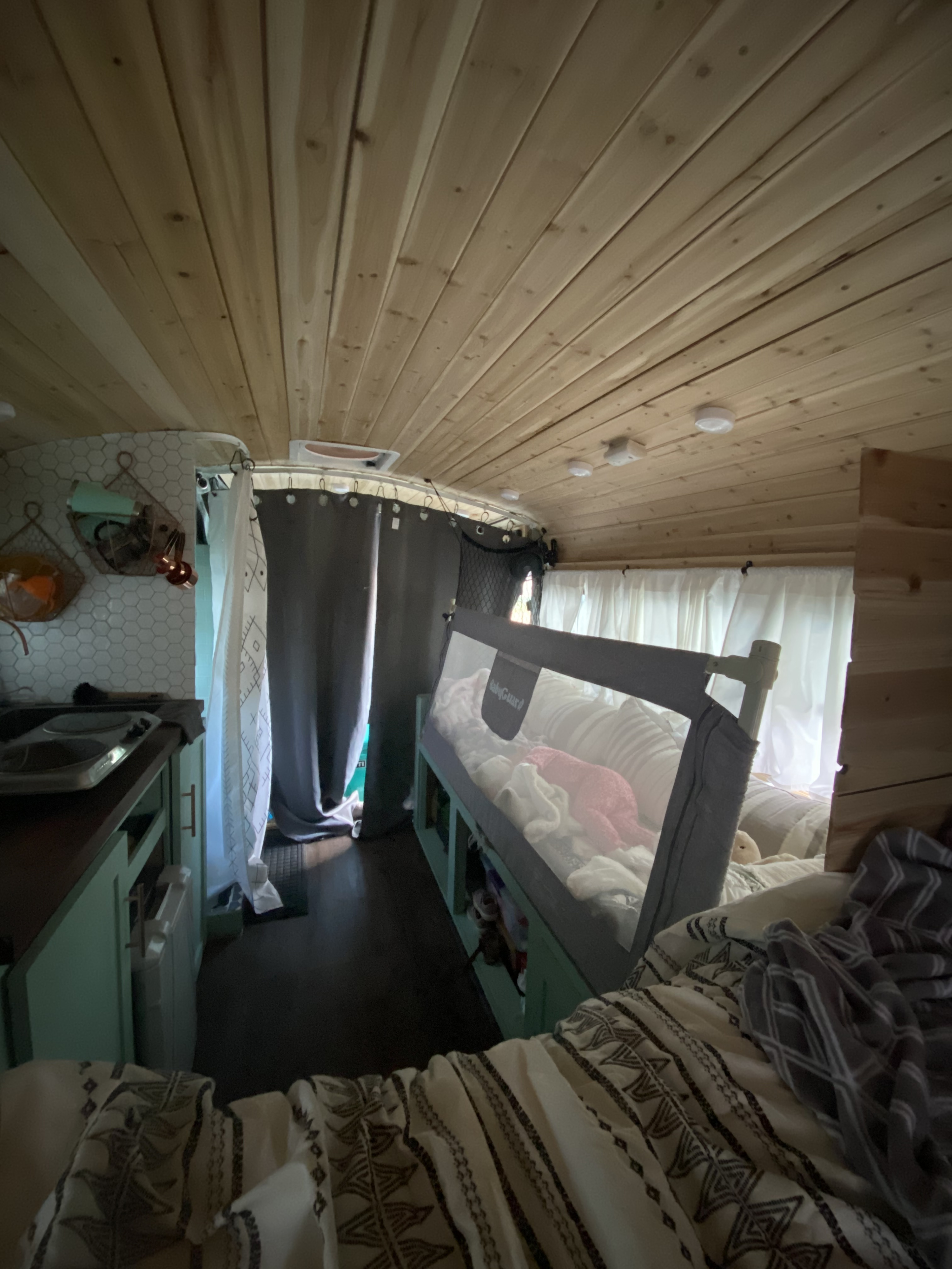 Cozy RV rental interior with kitchenette, baby bed rail, and warm wood ceiling. Perfect for family adventures.. Gmc Bus 2000