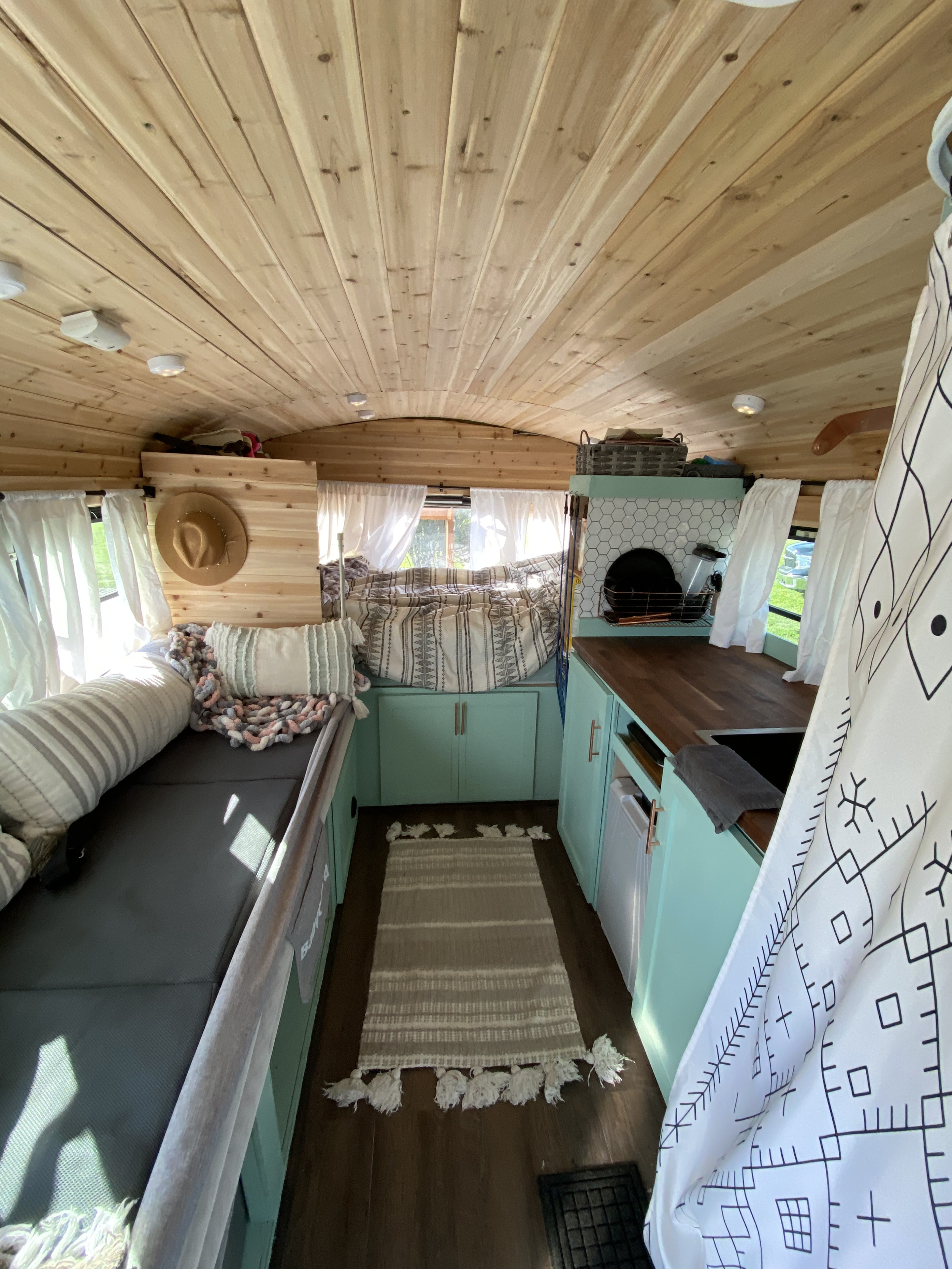 Cozy RV rental interior with wood plank ceiling, mint cabinets, and a comfy bed/living area.. Gmc Bus 2000