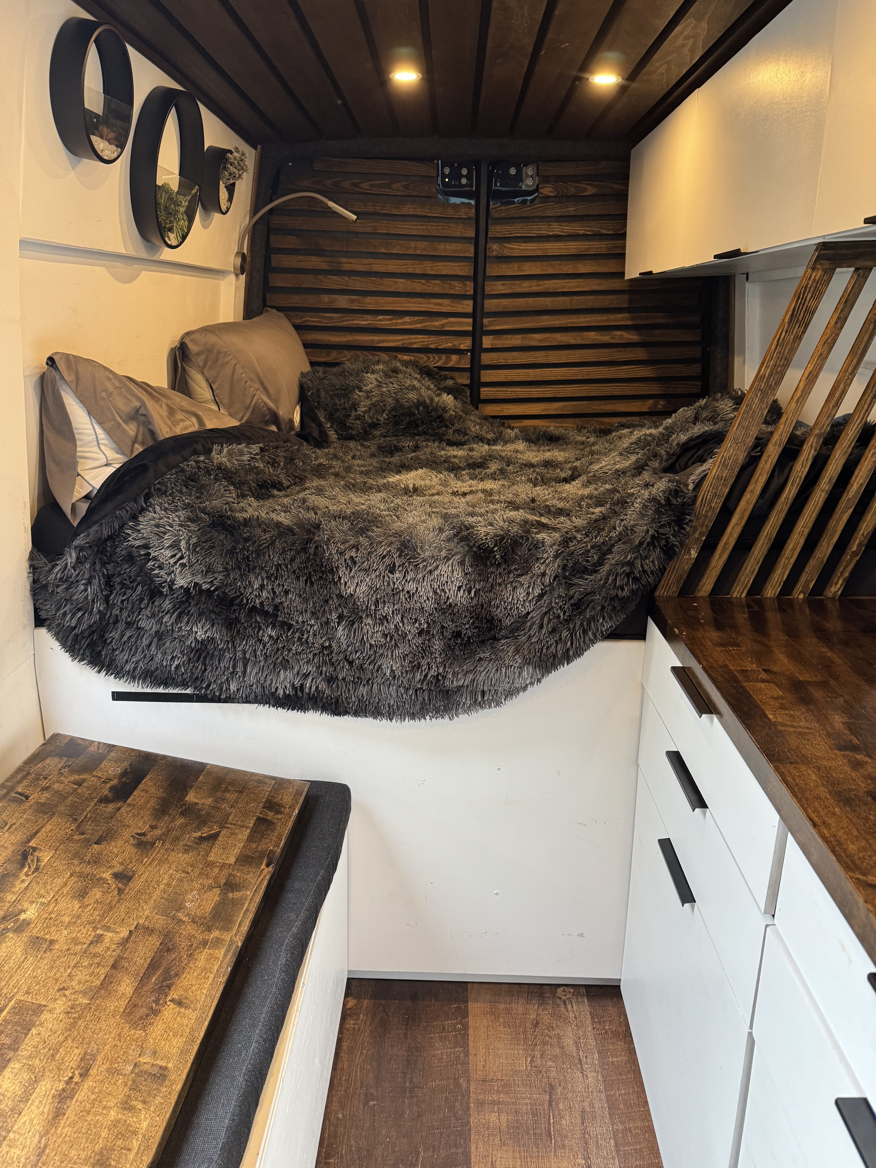 Cozy RV rental interior featuring a comfy bed, warm wood accents, and sleek white cabinetry.. Mercedes-Benz Sprinter 2020