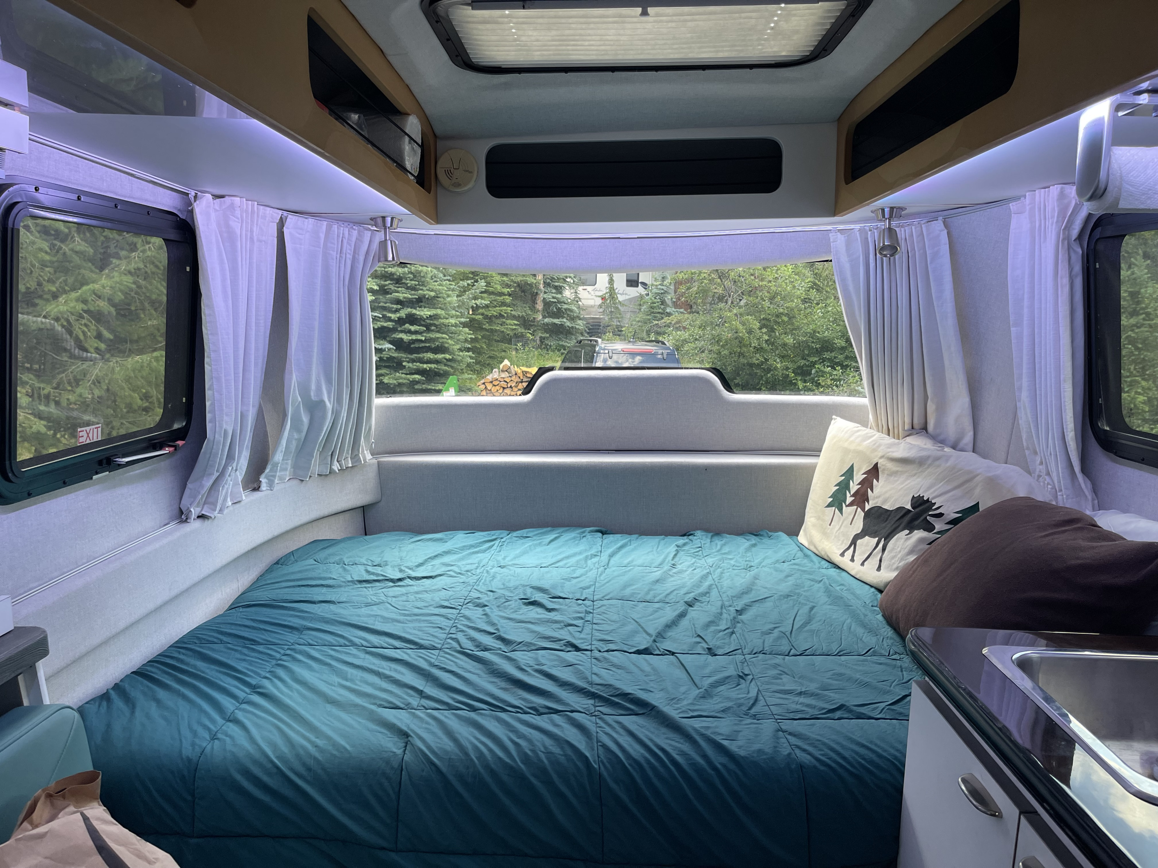 Cozy RV rental interior with a comfortable bed, compact kitchen, and scenic outdoor views through windows.. Airstream Nest 2018