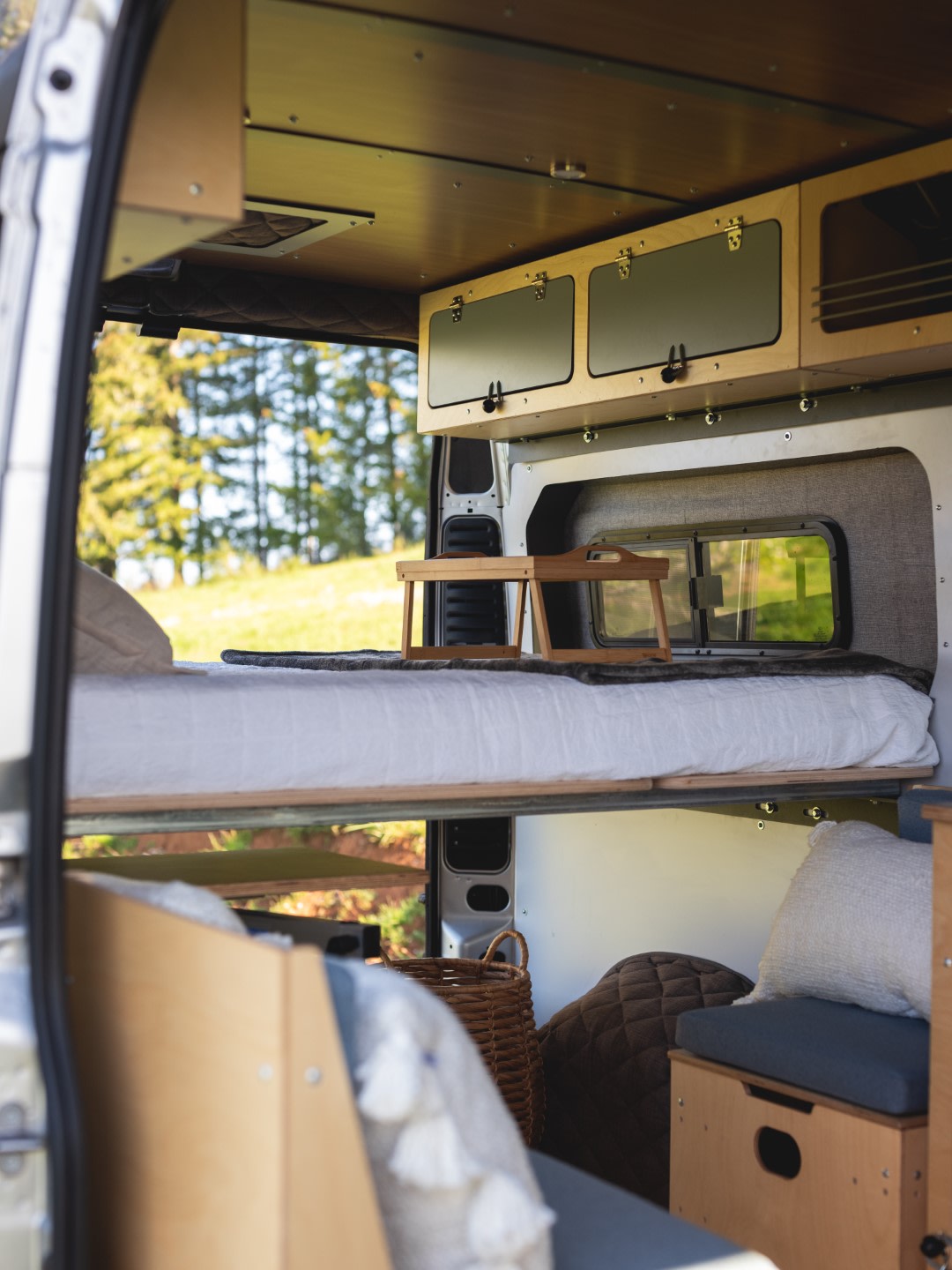 Inside a spacious RV rental camper van with a raised bed, wooden overhead storage, and lower living area seating.. Wayfarer Walt 2021