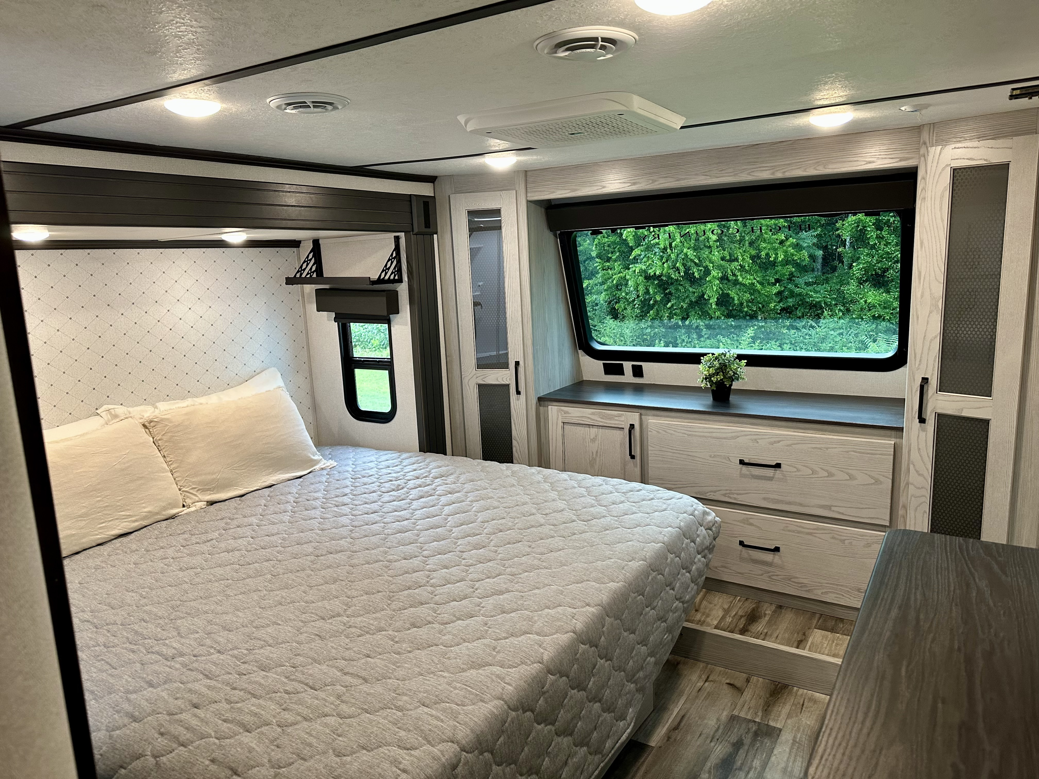 Experience comfort in this modern RV rental bedroom: cozy bed, large window with nature view, and storage.. Keystone RV Montana High Country 2022