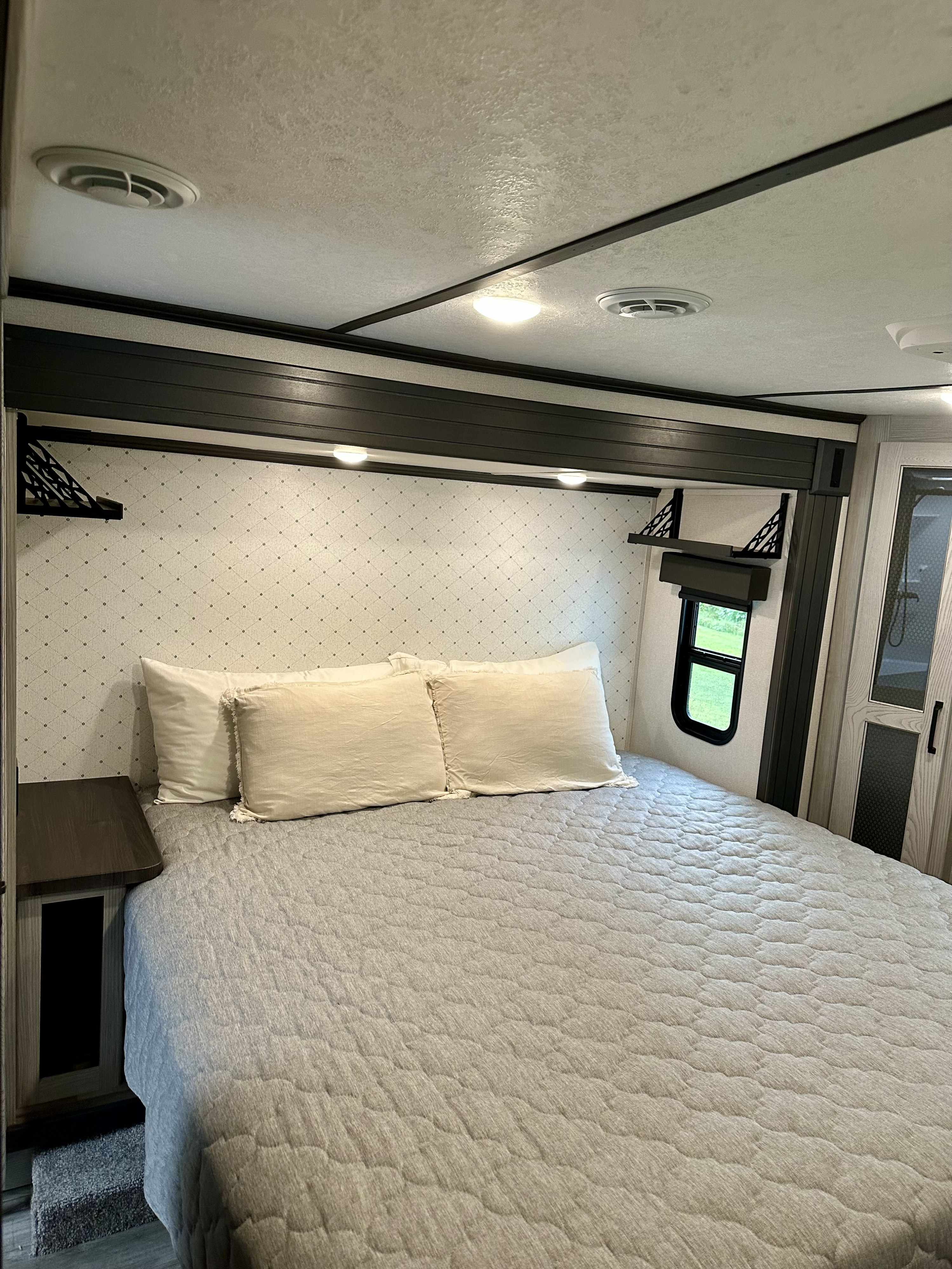 Bright, clean RV rental bedroom with a quilted bed, patterned headboard, window, and built-in storage/lights.. Keystone RV Montana High Country 2022