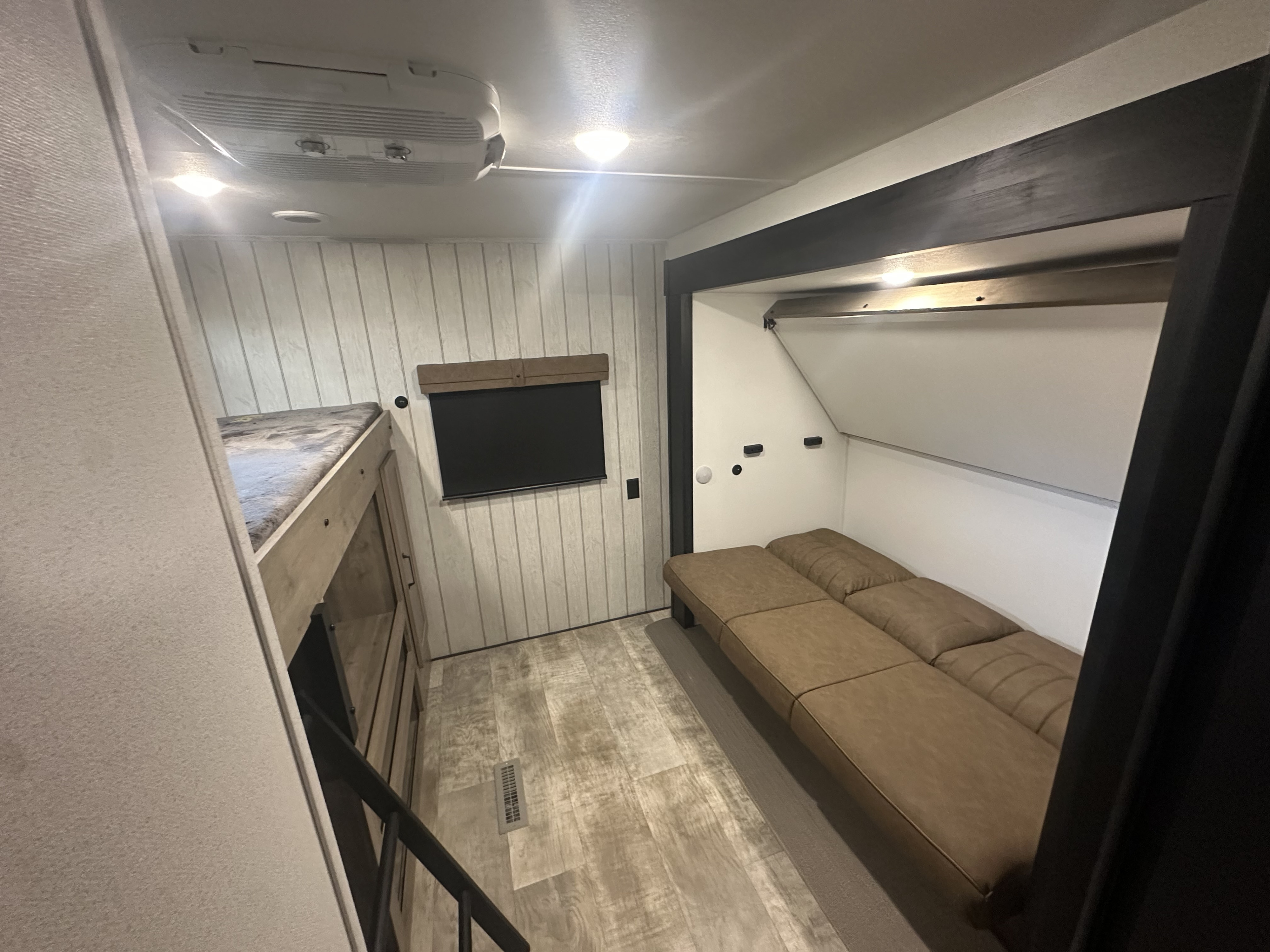 Spacious RV rental interior with light walls, bunk beds, a brown modular sofa, and entertainment screen.. Forest River Palomino Puma 31QBBH 2025
