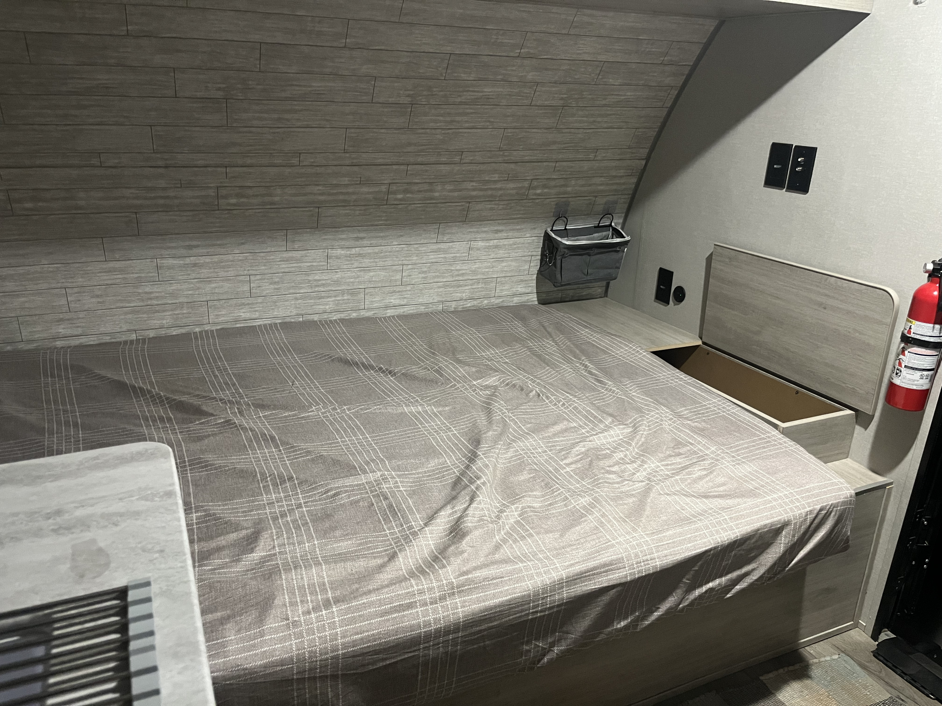 An RV rental bedroom featuring a plaid bed, integrated storage, and a fire extinguisher for safety and comfort.. Forest River Coachman Catalina 2025