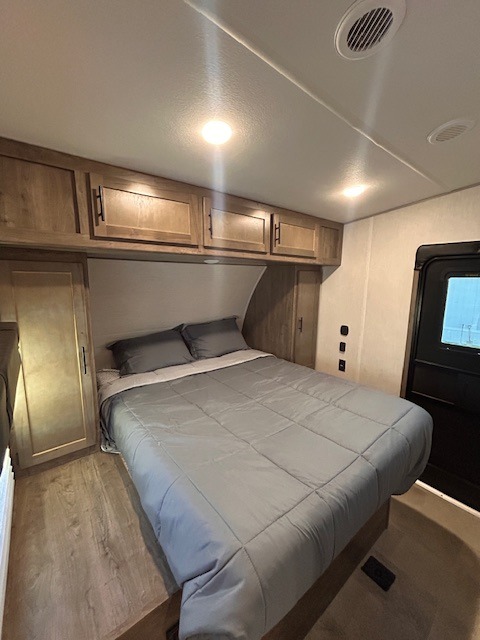 View of a spacious RV rental bedroom featuring a full bed with gray linens, ample overhead storage, and ceiling vents.. Forest River Vengeance 2022