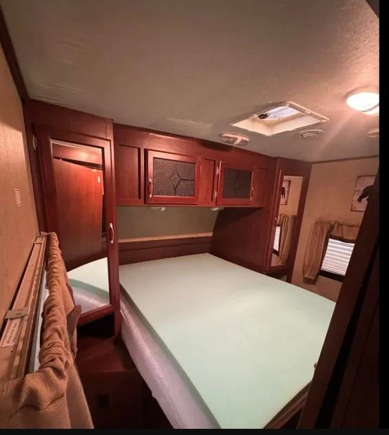 RV rental bedroom interior with a bed, light green foam topper, wood cabinets, and a ceiling skylight.. Evergreen RV Sun Valley 2014