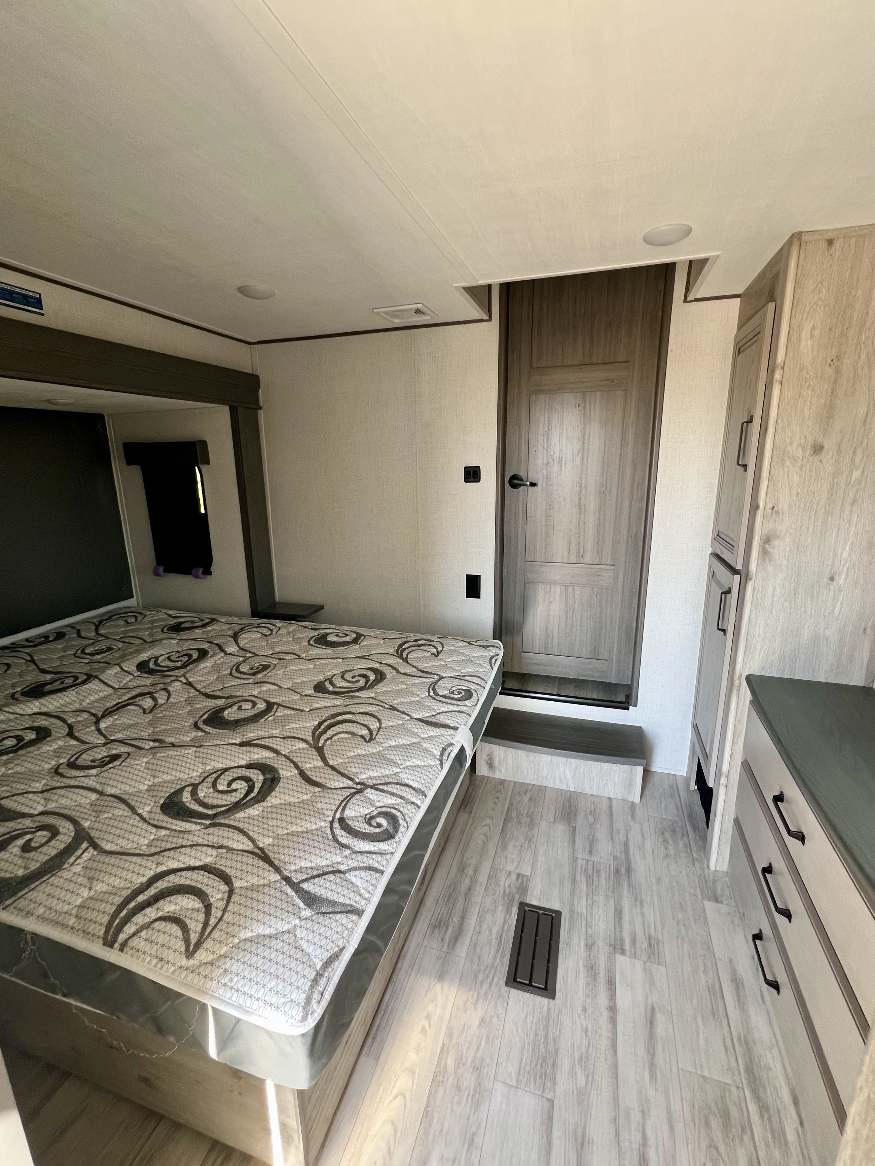 Modern RV rental bedroom. Features a large patterned bed, light wood floors, built-in storage cabinets, and a private door.. Keystone RV Alpine Avalanche 2024